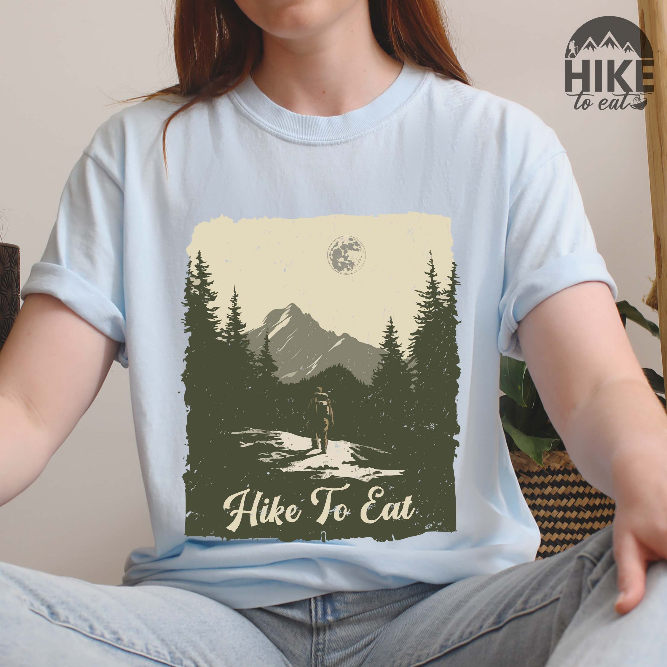 Woman wearing chambray "Hike to Eat" colored vintage tee with bold typography, illustrated landscape, and backpacker for burger enthusiasts.