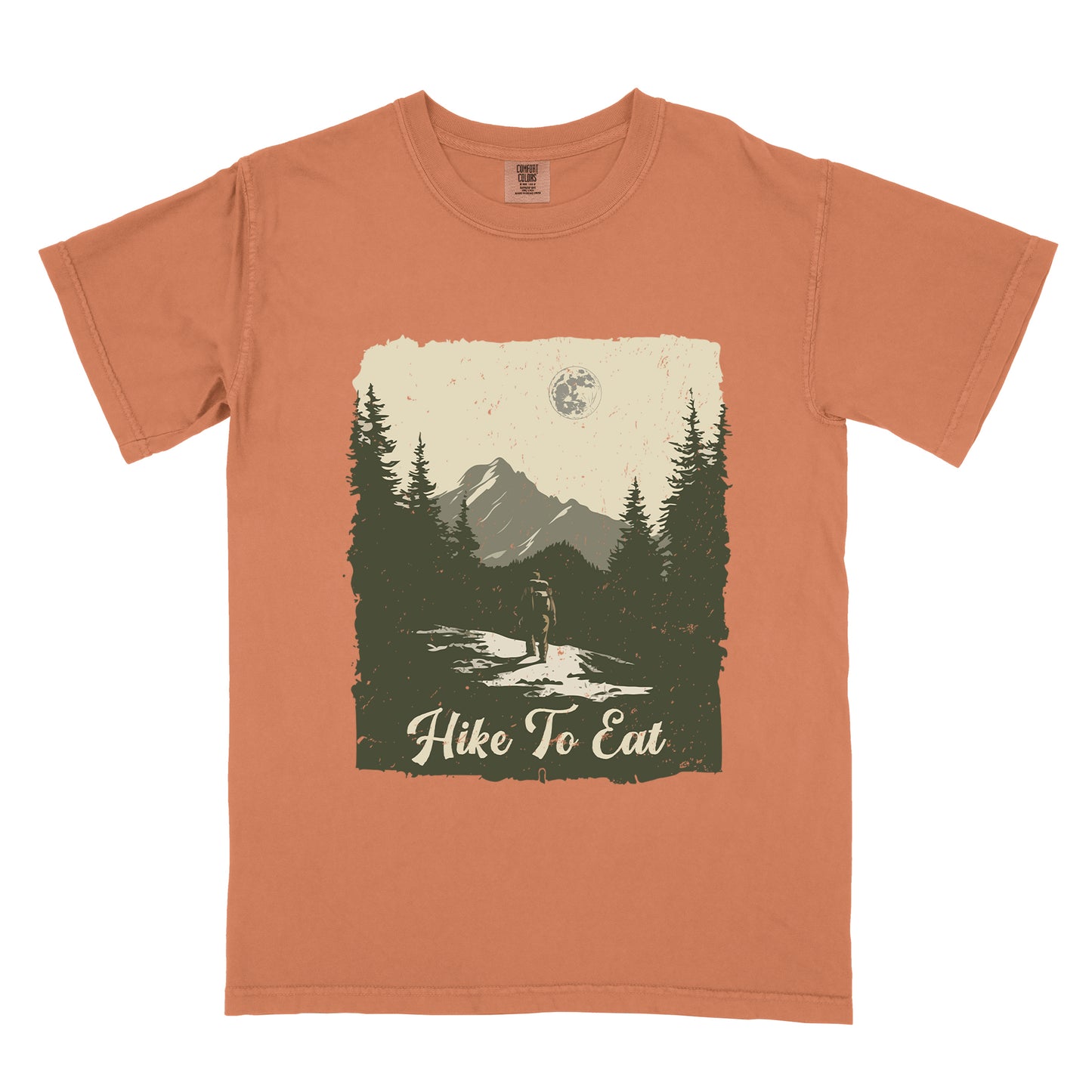 Yam (Brown) t-shirt featuring a vintage-style illustration of a lone hiker on a mountain trail. The rectangular design shows pine trees, mountain silhouettes, and a full moon against a cream-colored sky. A solitary hiker with backpack stands on the path facing the mountains. "Hike To Eat" appears in cream script at the bottom of the illustration. The artwork uses muted green, cream, and gray tones in a distressed, rustic style.