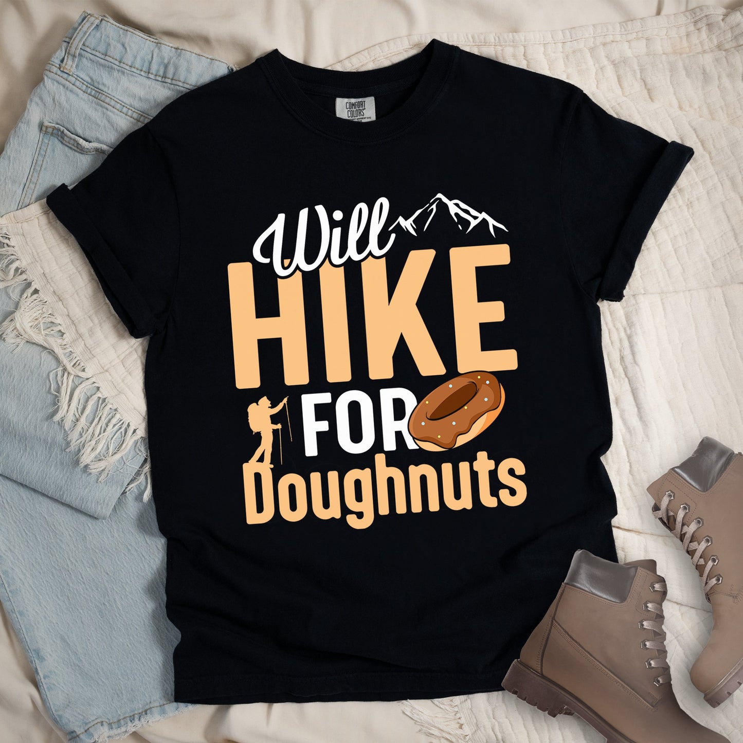 Black t-shirt with 'Will Hike for Doughnuts' design on a textured surface with jeans and hiking boots.