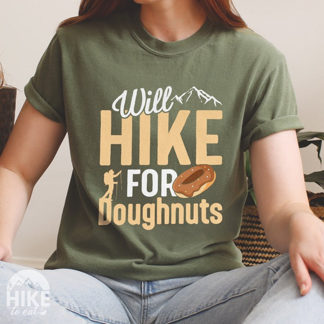 Woman wearing moss (green) Will Hike for Doughnuts statement t-shirt featuring chocolate doughnut graphic, mountain peaks, and hiker silhouette for doughnut lovers and outdoor enthusiasts on Comfort Colors 1717