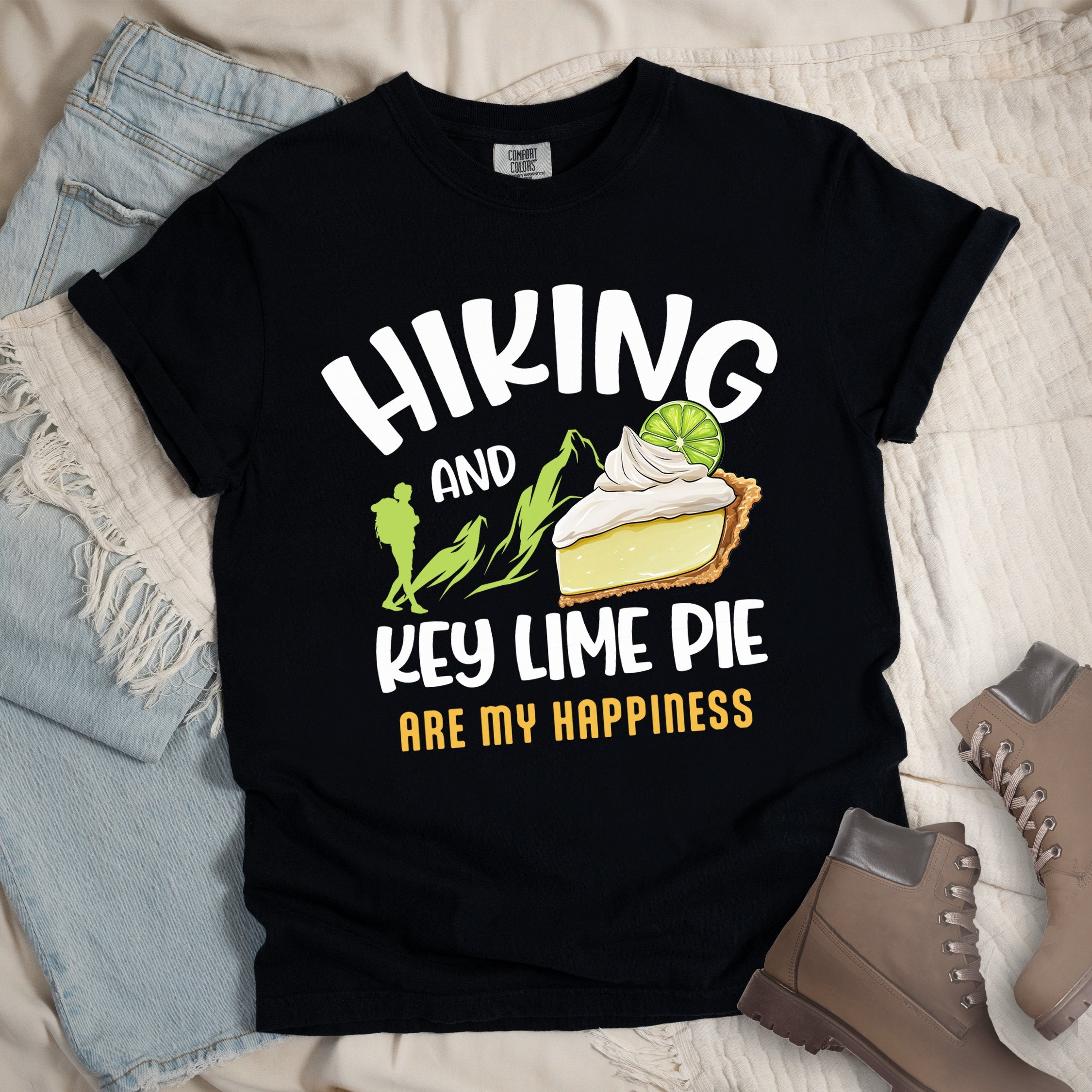 Black shirt with Hiking Design featuring the phrase “Hiking and Key Lime Pie Are My Happiness” and an illustration of a key lime pie slice topped with whipped cream and a lime slice beside green mountain graphics.