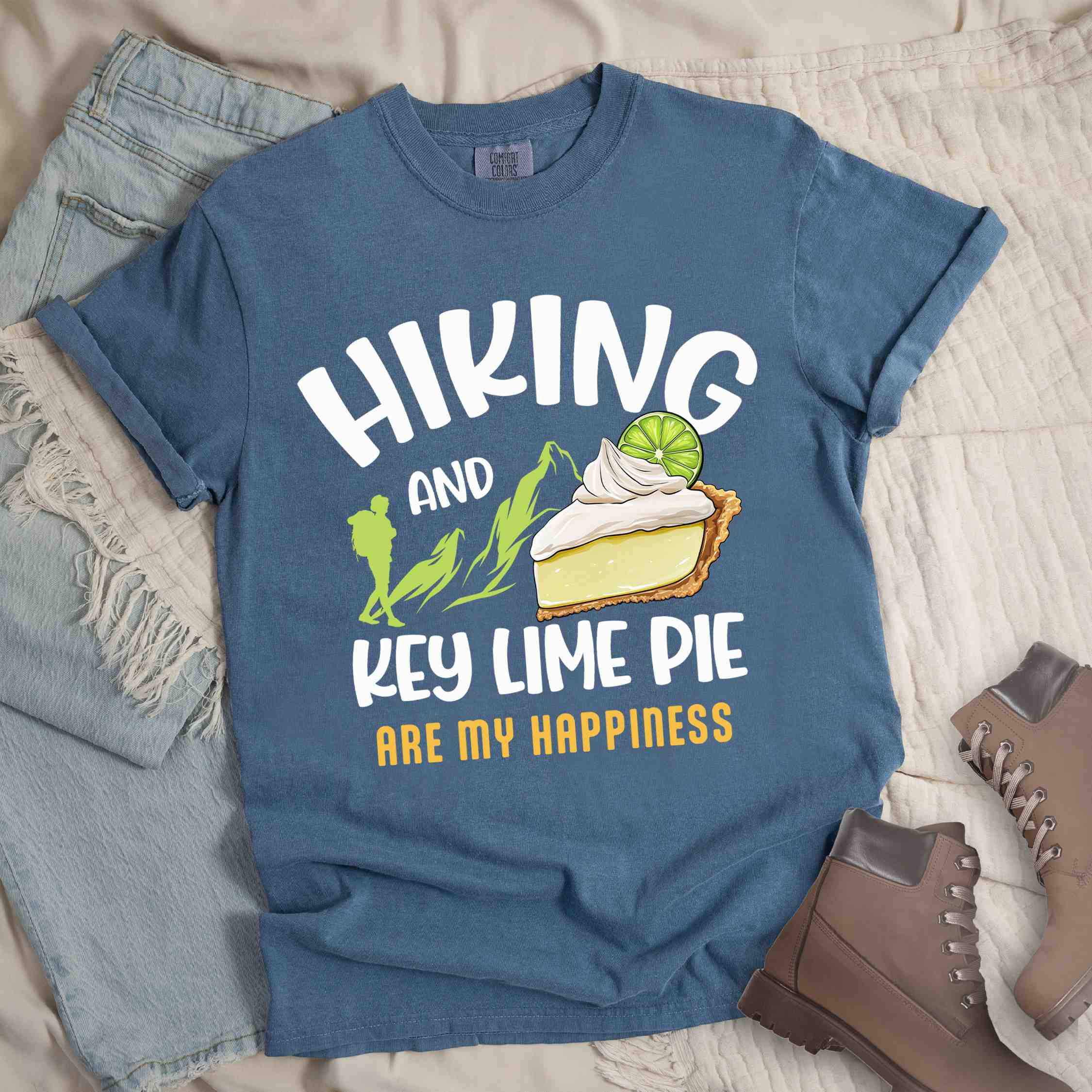 Blue jean "Hiking and key lime pie are my happiness" colored vintage tee with bold typography, mountains, birds, illustrated slice of key lime pie, and backpacker for pie lovers.
