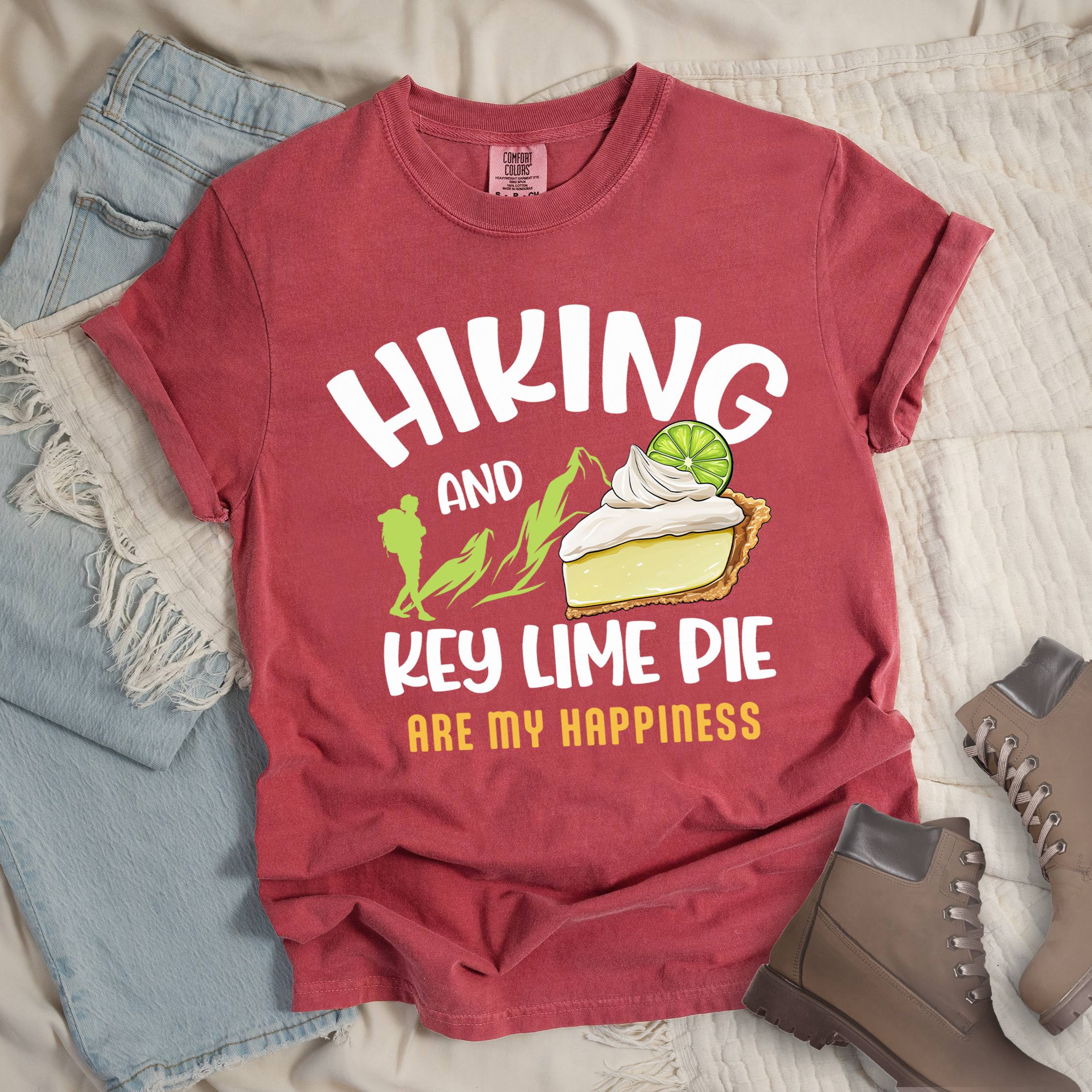 Red shirt with Hiking Design featuring the phrase “Hiking and Key Lime Pie Are My Happiness” and an illustration of a key lime pie slice topped with whipped cream and a lime slice beside green mountain graphics.