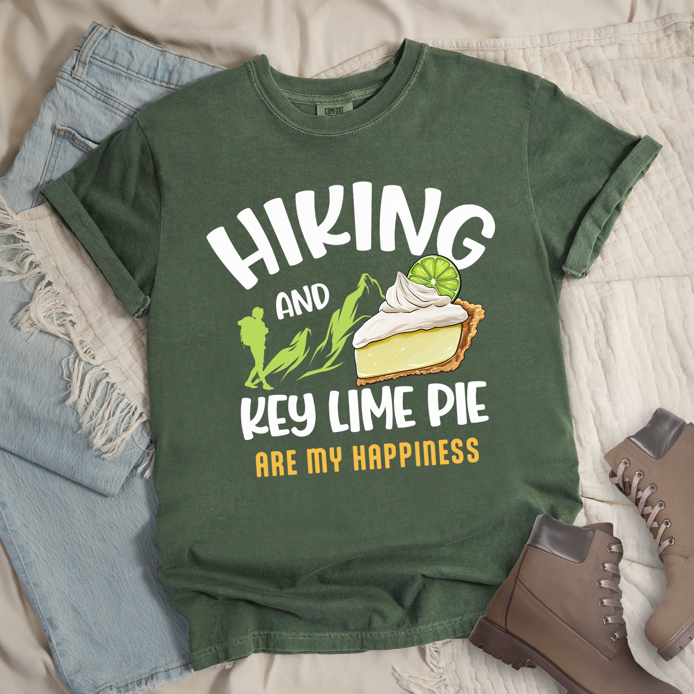 Dark green shirt with Hiking Design featuring the phrase “Hiking and Key Lime Pie Are My Happiness” and an illustration of a key lime pie slice topped with whipped cream and a lime slice beside green mountain graphics.