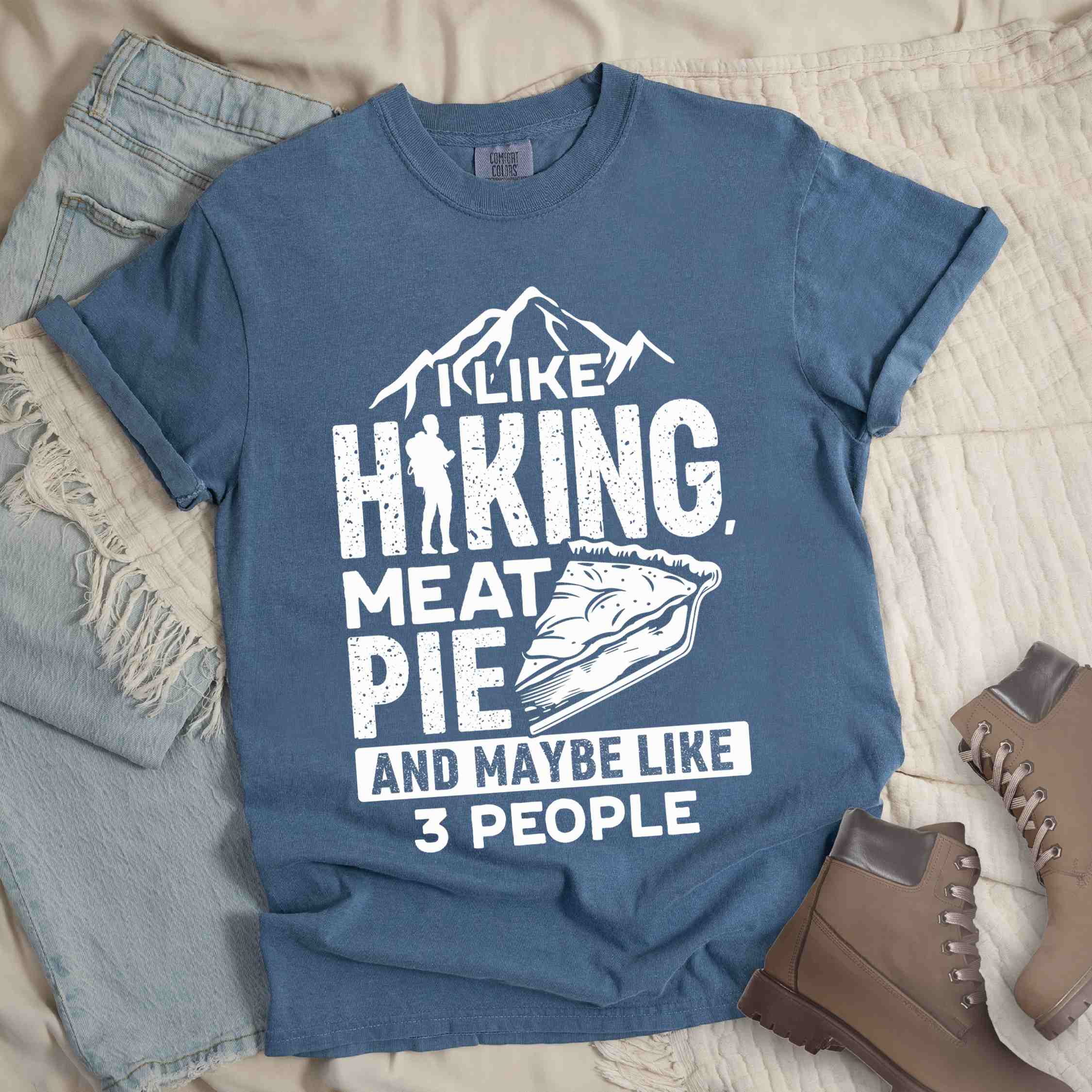 Blue jean "I like hiking, meat pie and maybe like 3 people" colored vintage tee with bold typography, mountains, birds, illustrated slice of meat pie, and backpacker for pie lovers.