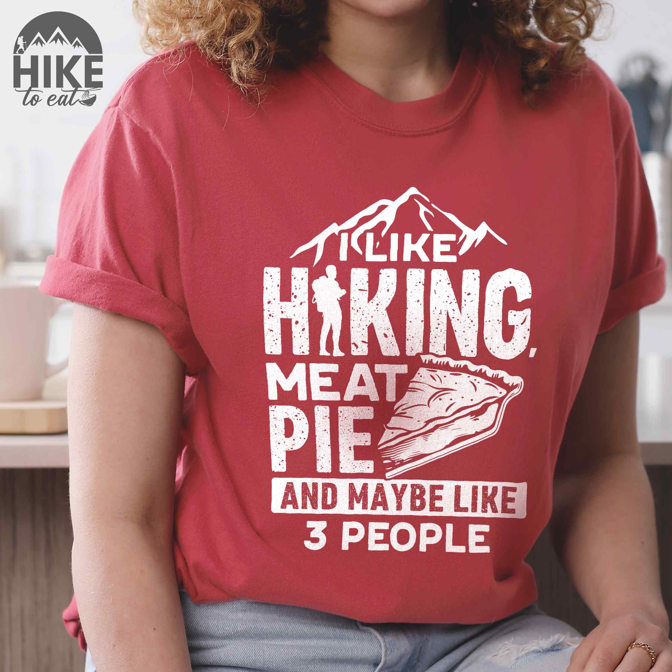 woman wearing crimson "I like hiking, meat pie and maybe like 3 people" colored vintage tee with bold typography, mountains, birds, illustrated slice of meat pie, and backpacker for pie lovers.