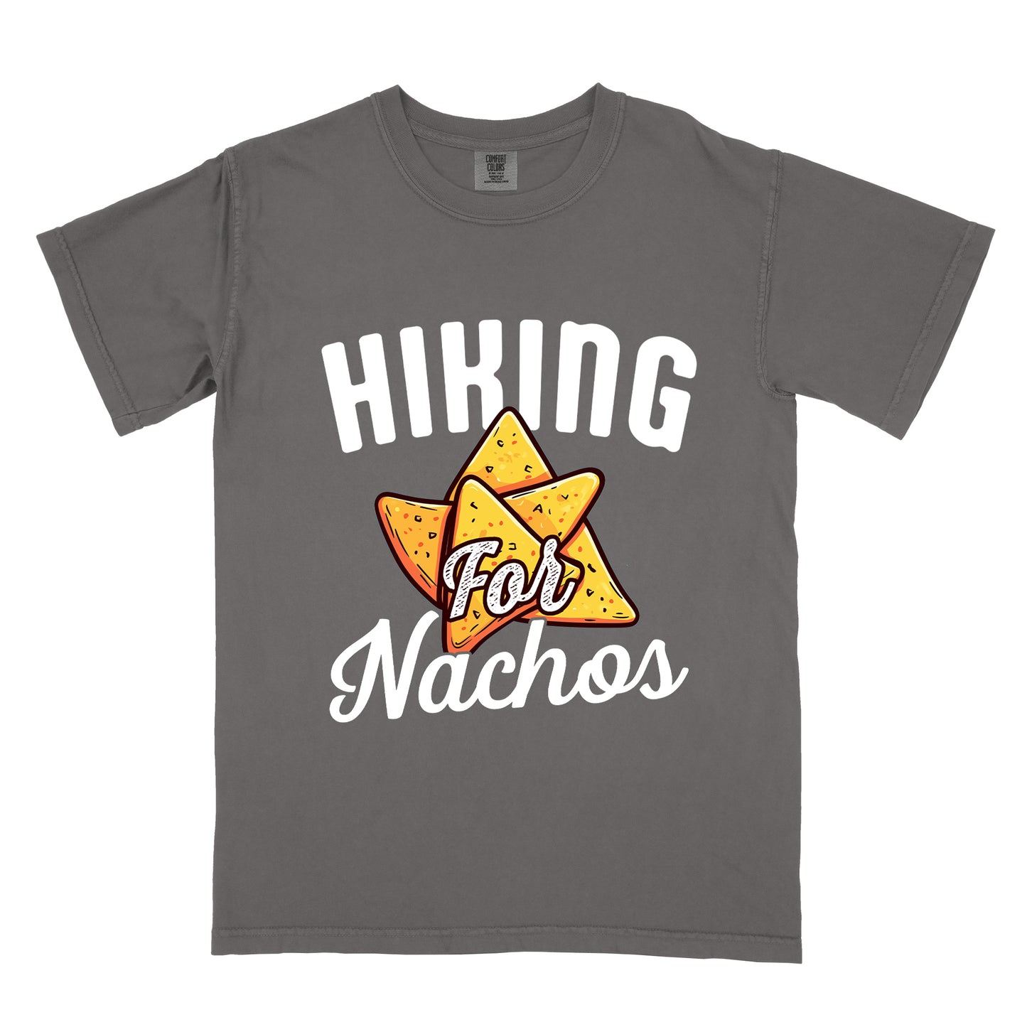 Pepper (Dark Gray) t-shirt with white text reading "HIKING For Nachos". "HIKING" appears in large white letters at the top, "For" in white script across the middle, and "Nachos" in white script at the bottom. The centerpiece of the design is an illustration of tortilla chips arranged in a star-like pattern, colored yellow-orange with flecks to represent seasonings. The design connects hiking activity with food motivation.