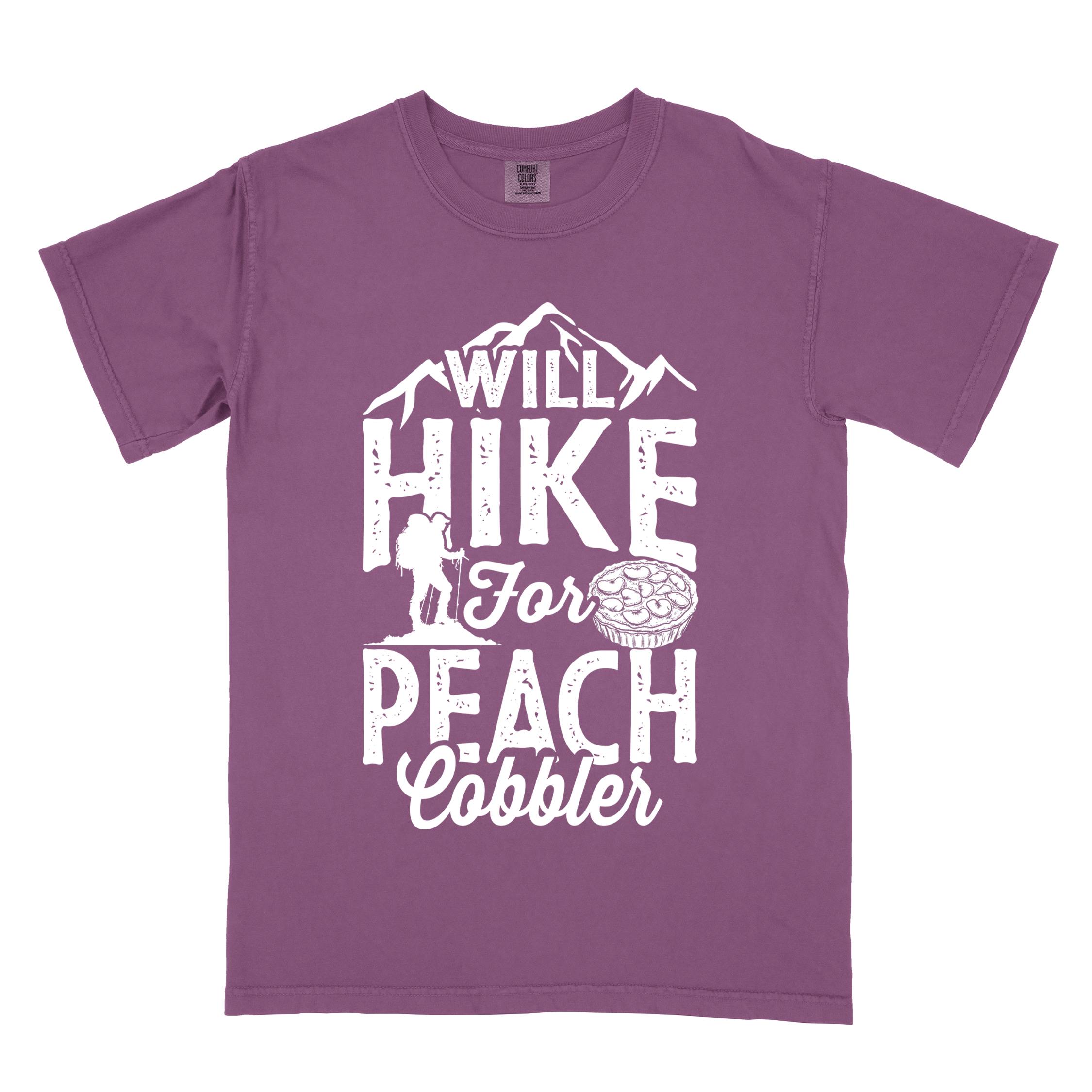 Berry "Will hike for peach cobbler" colored vintage tee with bold typography, mountain, birds, illustrated peach cobbler, and backpacker looking for sweet treats.