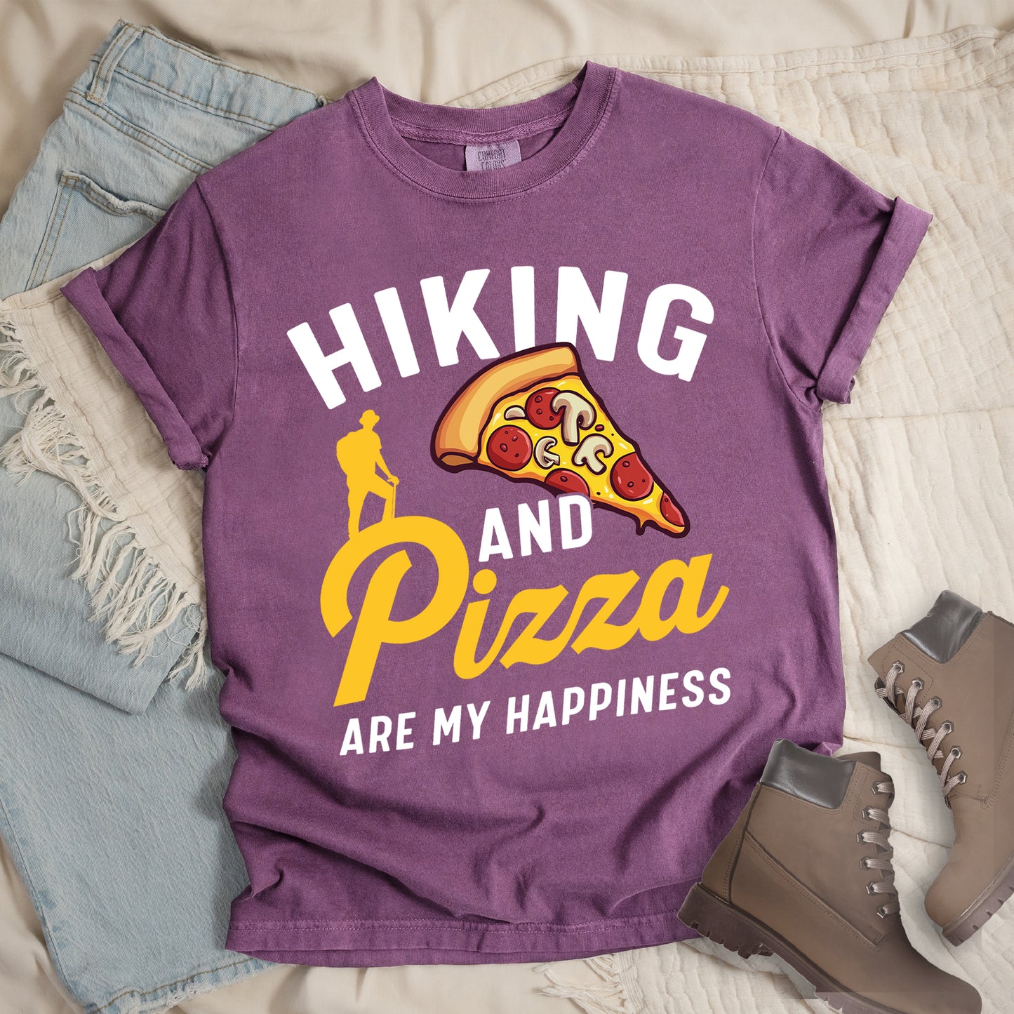 Berry (Dark Violet) t-shirt with white and yellow text reading "HIKING AND Pizza ARE MY HAPPINESS". "HIKING" appears in white at the top, "AND" in white in the middle, "Pizza" in yellow script, and "ARE MY HAPPINESS" in white at the bottom. Features a colorful pizza slice with pepperoni and mushrooms in the center-right and a yellow silhouette of a hiker on the left side above "AND Pizza ARE MY HAPPINESS". The design combines outdoor activity with food enjoyment.