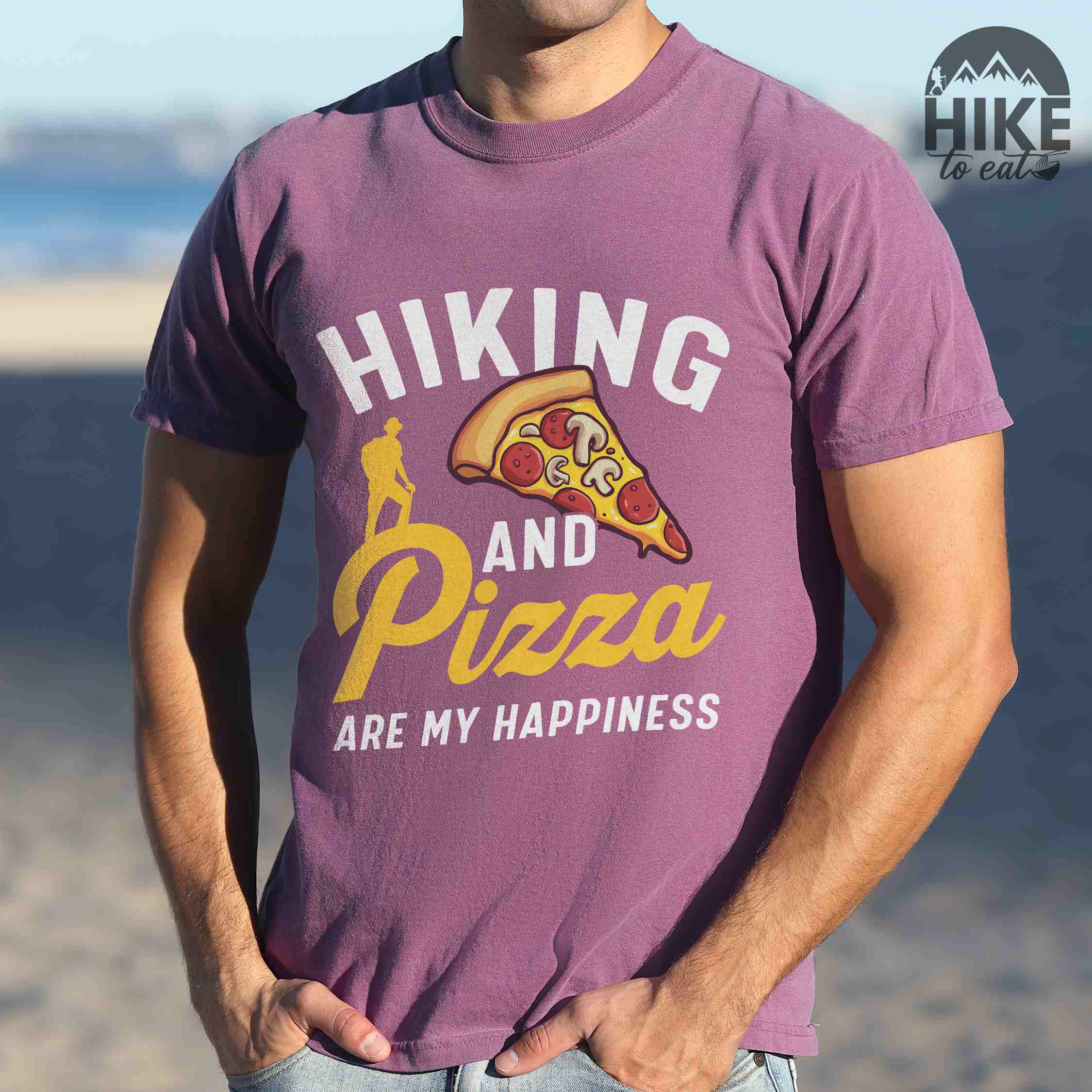 Man wearing berry "Hiking and Pizza are my happiness" colored vintage tee with bold typography, birds, mountains, illustrated pizza slice, and backpacker for pizza lovers.