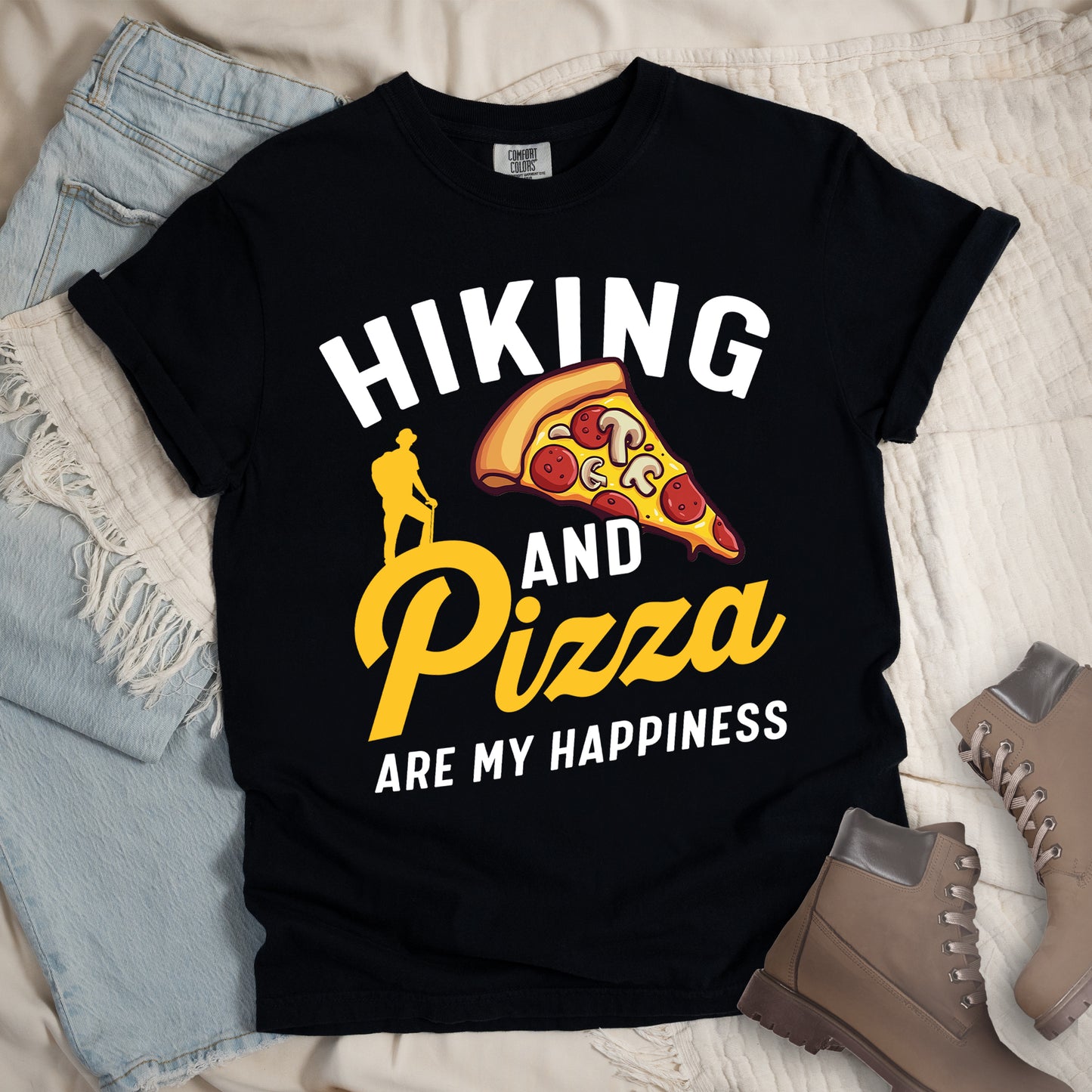 Black t-shirt with white and yellow text reading "HIKING AND Pizza ARE MY HAPPINESS". "HIKING" appears in white at the top, "AND" in white in the middle, "Pizza" in yellow script, and "ARE MY HAPPINESS" in white at the bottom. Features a colorful pizza slice with pepperoni and mushrooms in the center-right and a yellow silhouette of a hiker on the left side above "AND Pizza ARE MY HAPPINESS". The design combines outdoor activity with food enjoyment.