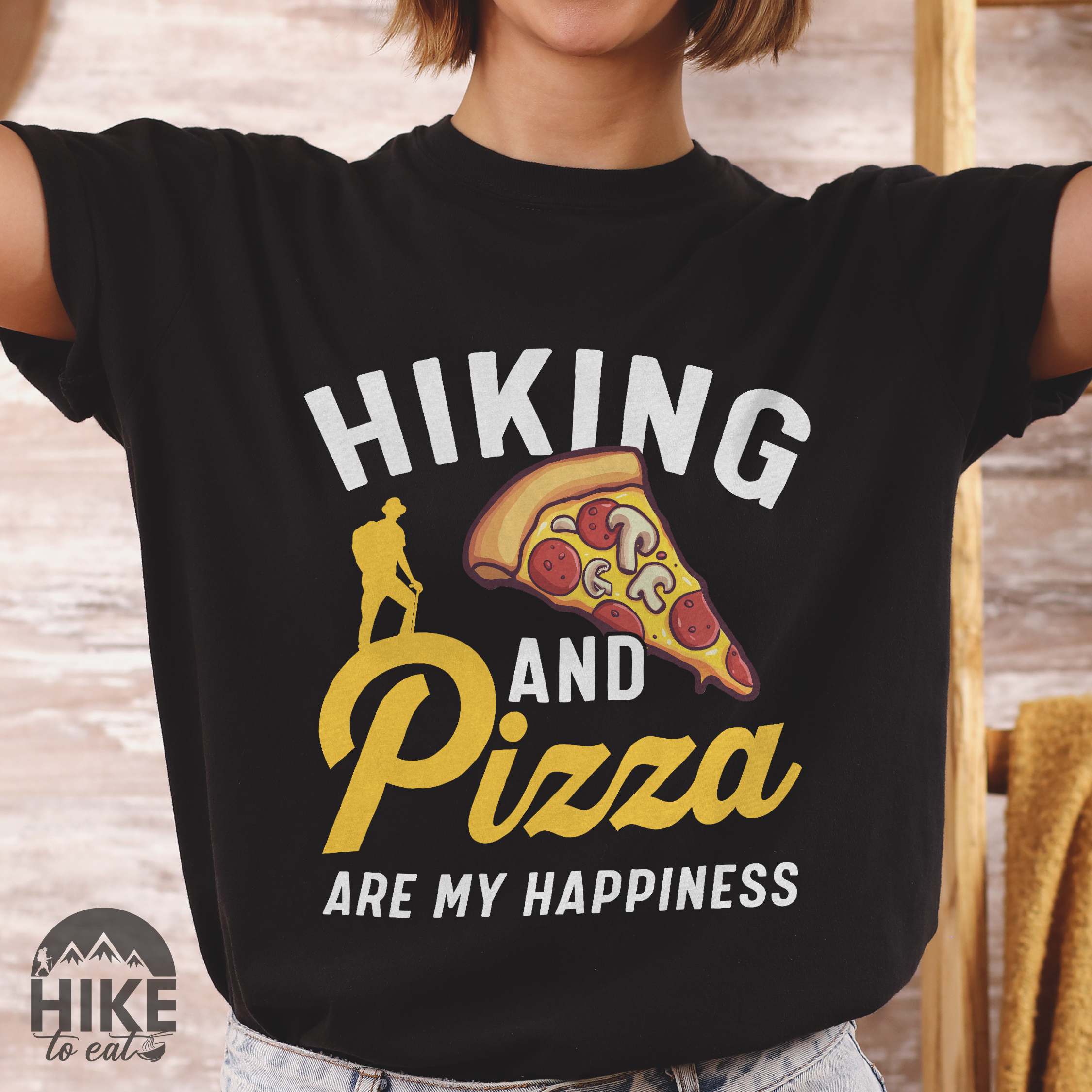 woman wearing black "Hiking and Pizza are my happiness" colored vintage tee with bold typography, birds, mountains, illustrated pizza slice, and backpacker for pizza lovers.