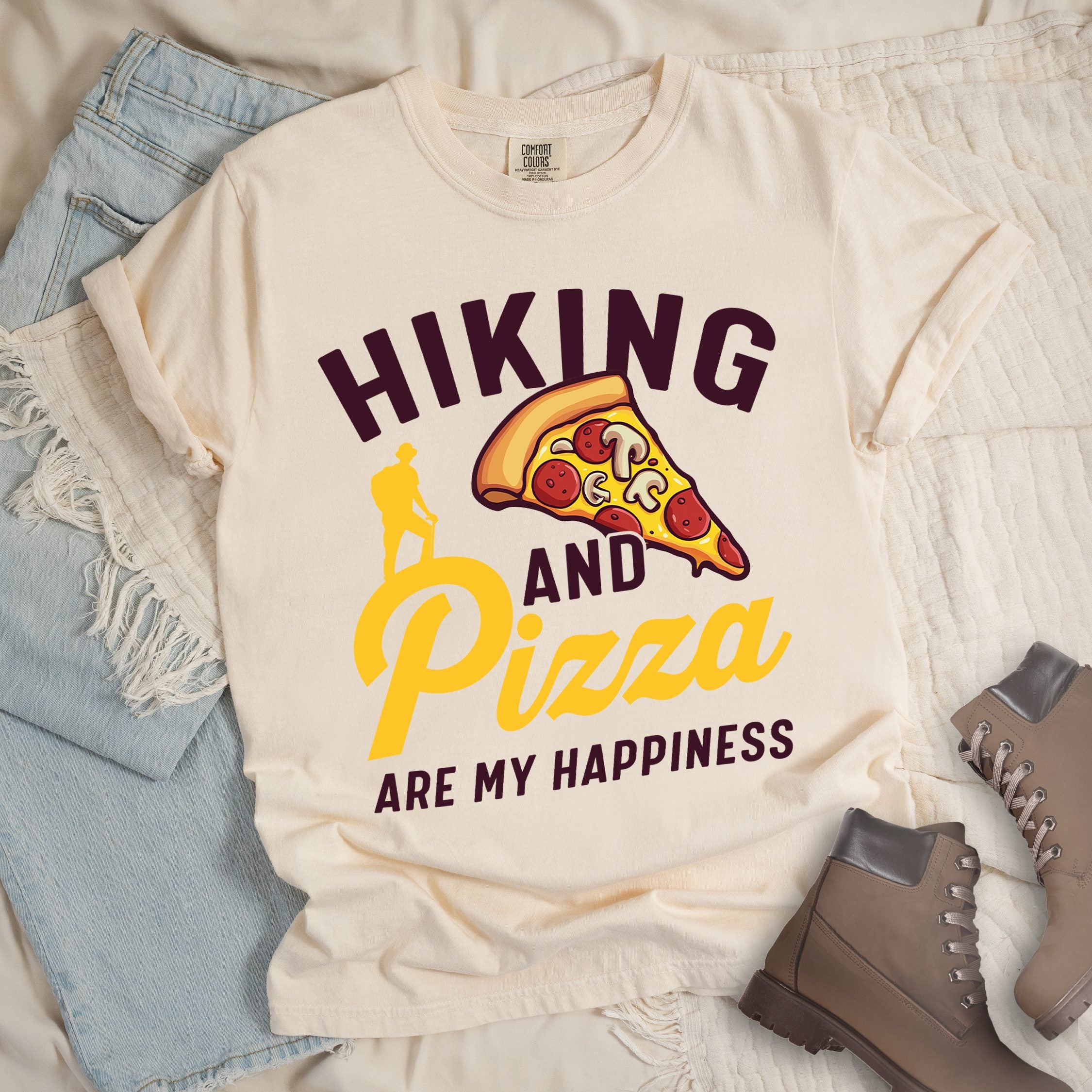Ivory shirt with Hiking Design featuring the phrase “Hiking and Pizza Are My Happiness” and an illustration of a pepperoni pizza slice with a hiker silhouette beside it.