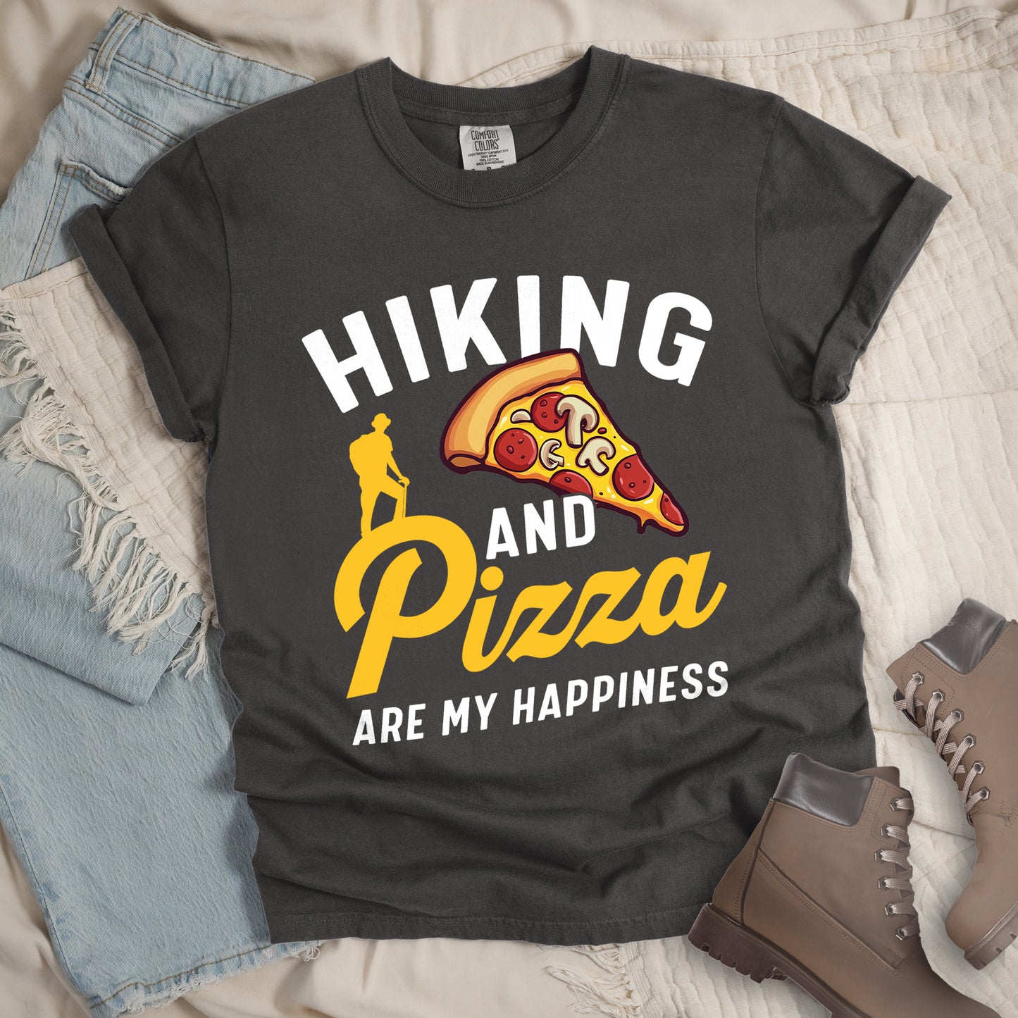 Pepper (Dark Gray) t-shirt with white and yellow text reading "HIKING AND Pizza ARE MY HAPPINESS". "HIKING" appears in white at the top, "AND" in white in the middle, "Pizza" in yellow script, and "ARE MY HAPPINESS" in white at the bottom. Features a colorful pizza slice with pepperoni and mushrooms in the center-right and a yellow silhouette of a hiker on the left side above "AND Pizza ARE MY HAPPINESS". The design combines outdoor activity with food enjoyment.
