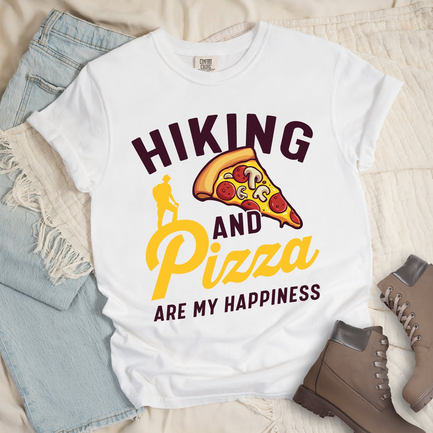 White t-shirt with deep brown and yellow text reading "HIKING AND Pizza ARE MY HAPPINESS". "HIKING" appears in deep brown at the top, "AND" in deep brown in the middle, "Pizza" in yellow script, and "ARE MY HAPPINESS" in deep brown at the bottom. Features a colorful pizza slice with pepperoni and mushrooms in the center-right and a yellow silhouette of a hiker on the left side above "AND Pizza ARE MY HAPPINESS". The design combines outdoor activity with food enjoyment.