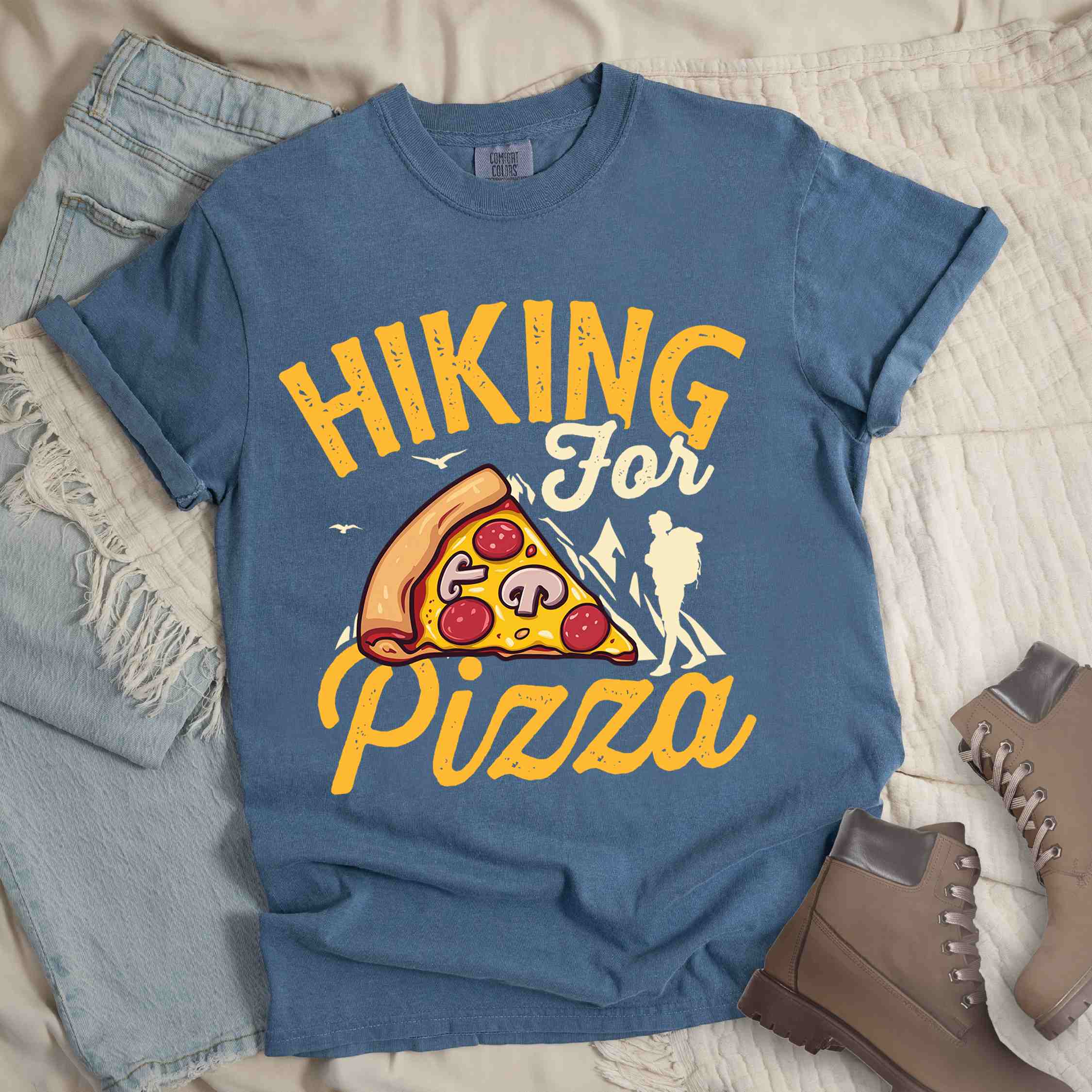 Blue jean "Hiking for Pizza" colored vintage tee with bold typography, birds, mountains, illustrated pizza slice, and backpacker for pizza lovers.