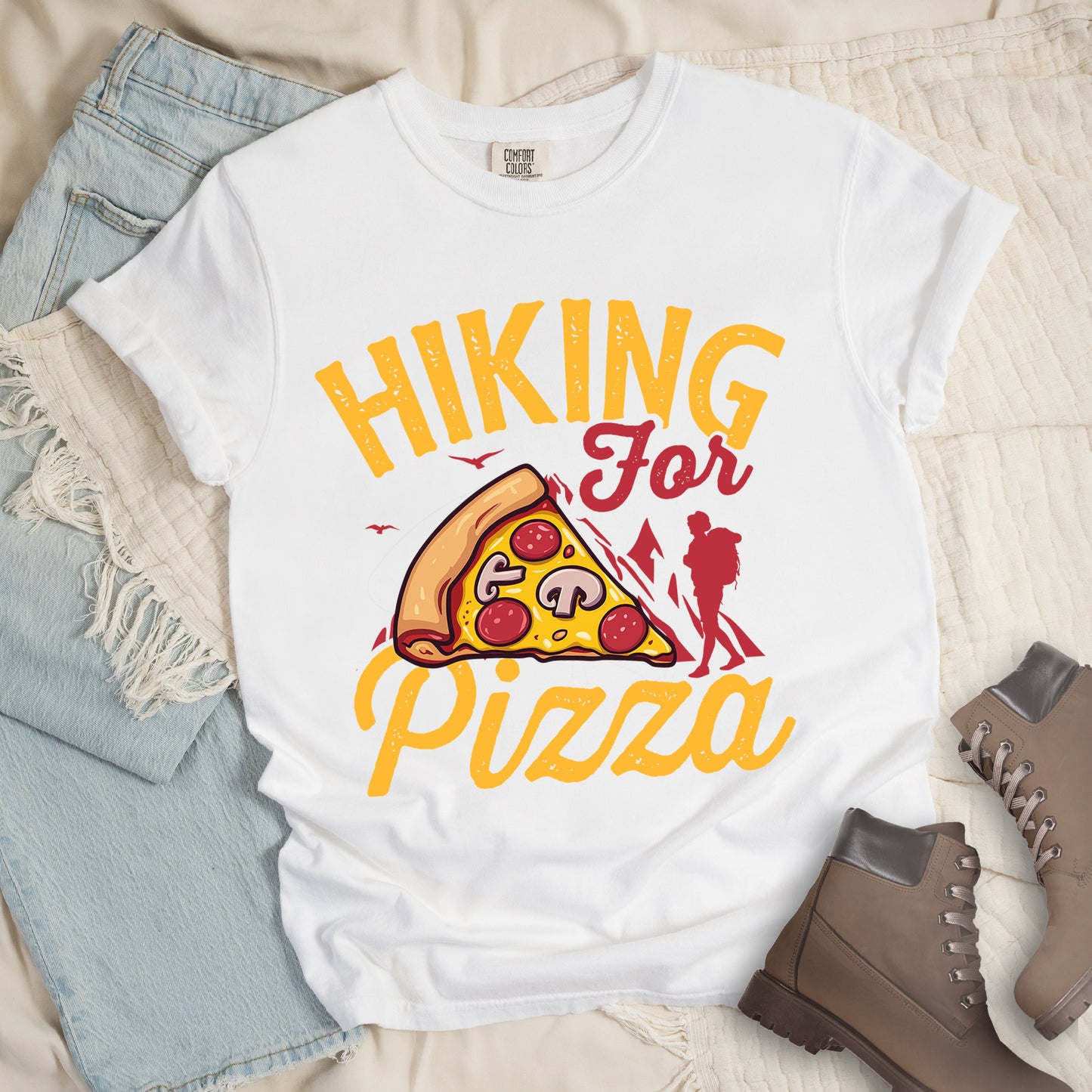 White t-shirt with yellow distressed text reading "HIKING For Pizza". "HIKING" appears in large yellow letters at the top, "For" in red script in the middle, and "Pizza" in yellow script at the bottom. Features a detailed pizza slice with pepperoni and mushrooms in the center and a red silhouette of a hiker on the right side against mountain outlines. Small bird silhouettes appear near the mountains. The design connects hiking activity with food reward.