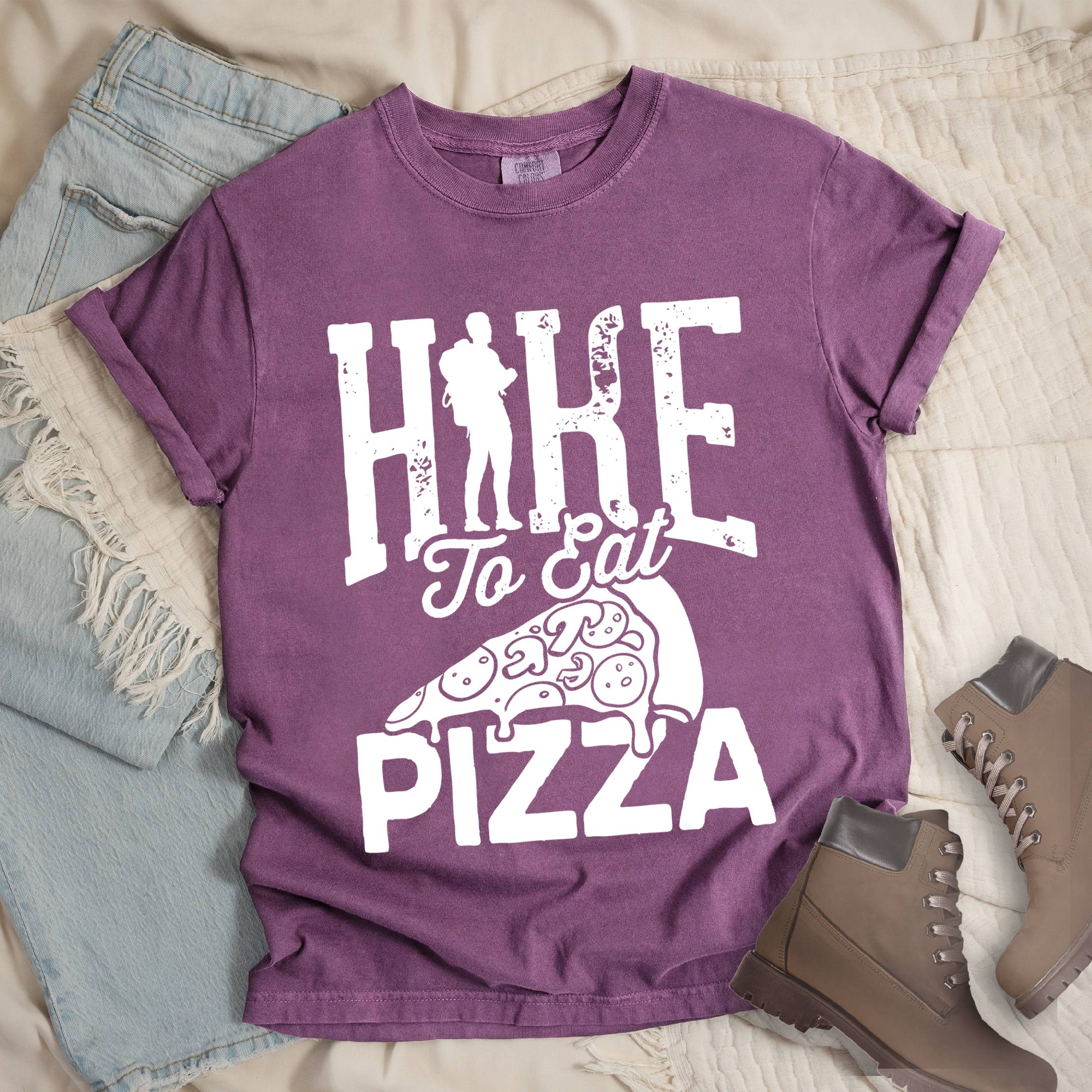 Dark pink shirt with Hiking Design featuring the phrase “Hike to Eat Pizza” with a bold hiker silhouette and an illustration of a large pizza slice.