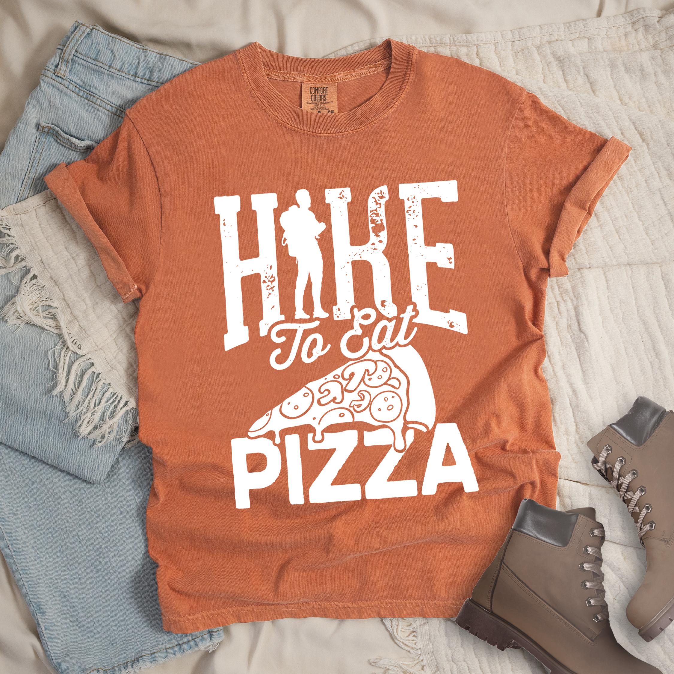 Orange shirt with Hiking Design featuring the phrase “Hike to Eat Pizza” with a bold hiker silhouette and an illustration of a large pizza slice.