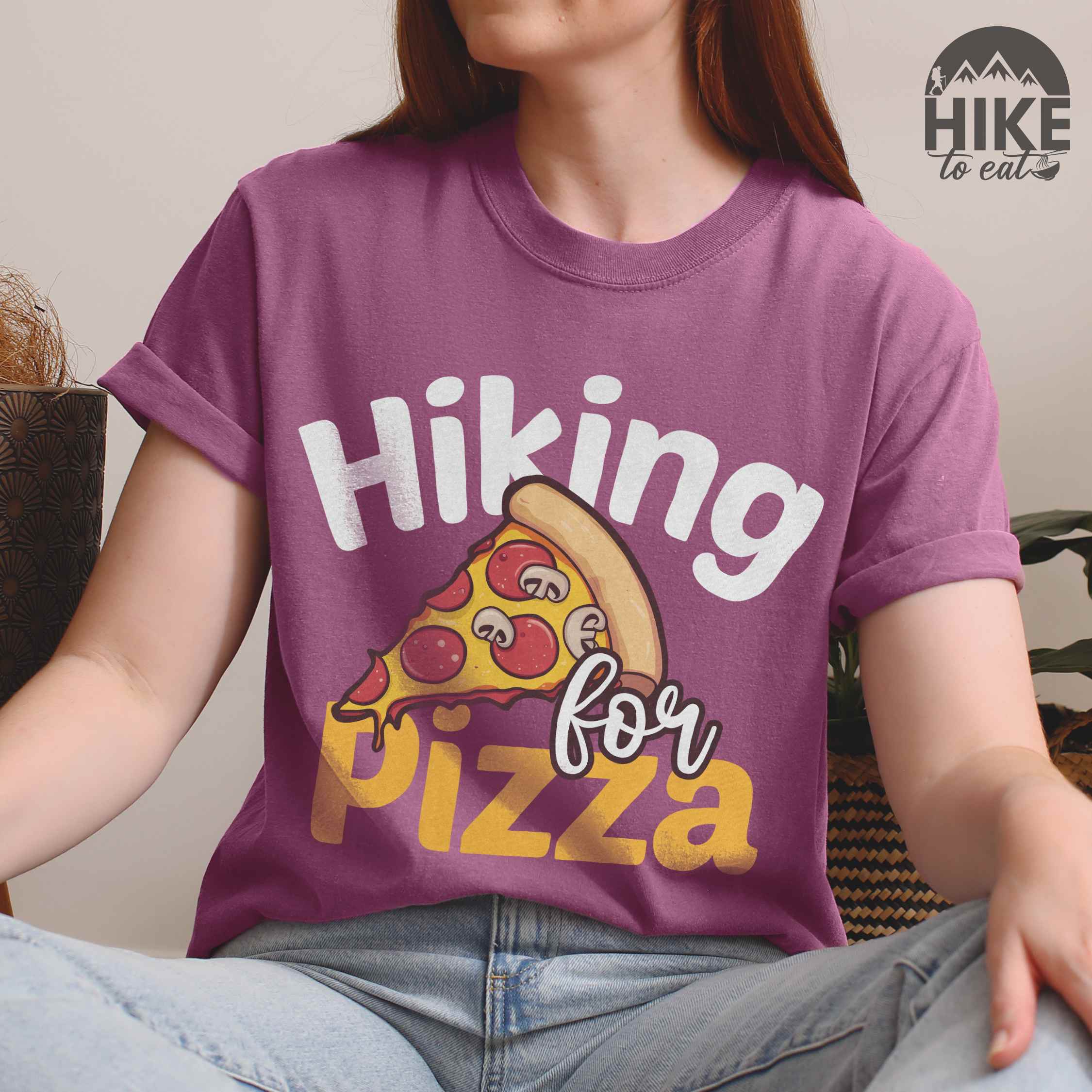 Woman wearing berry "Hiking for pizza" colored vintage tee with bold typography, illustrated pizza slice, and backpacker for pizza lover.
