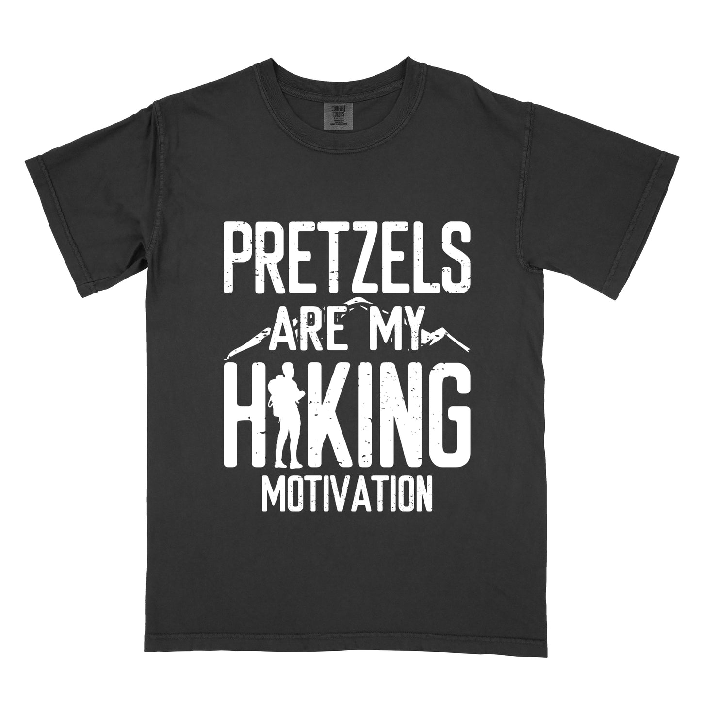 Black t-shirt with white distressed text reading "PRETZELS ARE MY HIKING MOTIVATION". "PRETZELS" appears at the top, "ARE MY" in the middle with small mountain silhouettes behind it, and "HIKING" in large letters with a hiker silhouette integrated into the letter "H". "MOTIVATION" appears at the bottom.