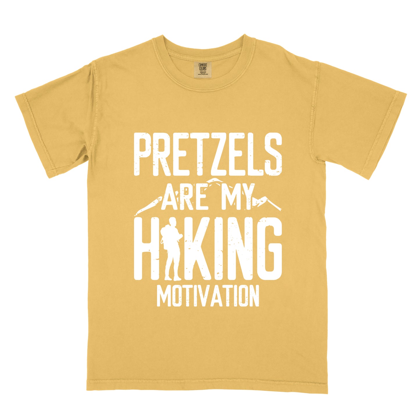 Mustard (Yellow) t-shirt with white distressed text reading "PRETZELS ARE MY HIKING MOTIVATION". "PRETZELS" appears at the top, "ARE MY" in the middle with small mountain silhouettes behind it, and "HIKING" in large letters with a hiker silhouette integrated into the letter "H". "MOTIVATION" appears at the bottom.