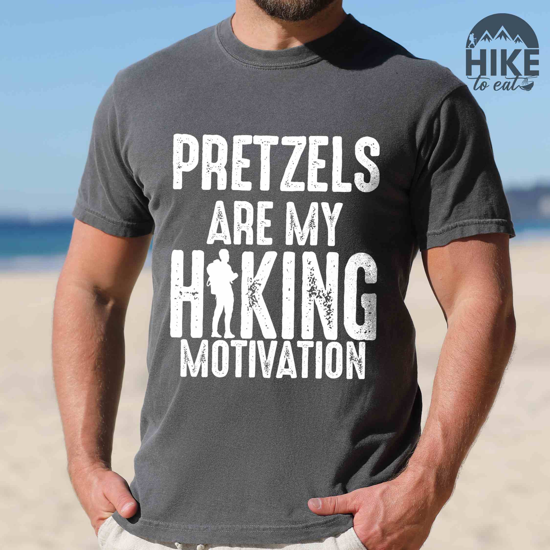 Man wearing pepper "Pretzels are my hiking motivation" colored vintage tee with bold typography, and backpacker for pretzel lovers.