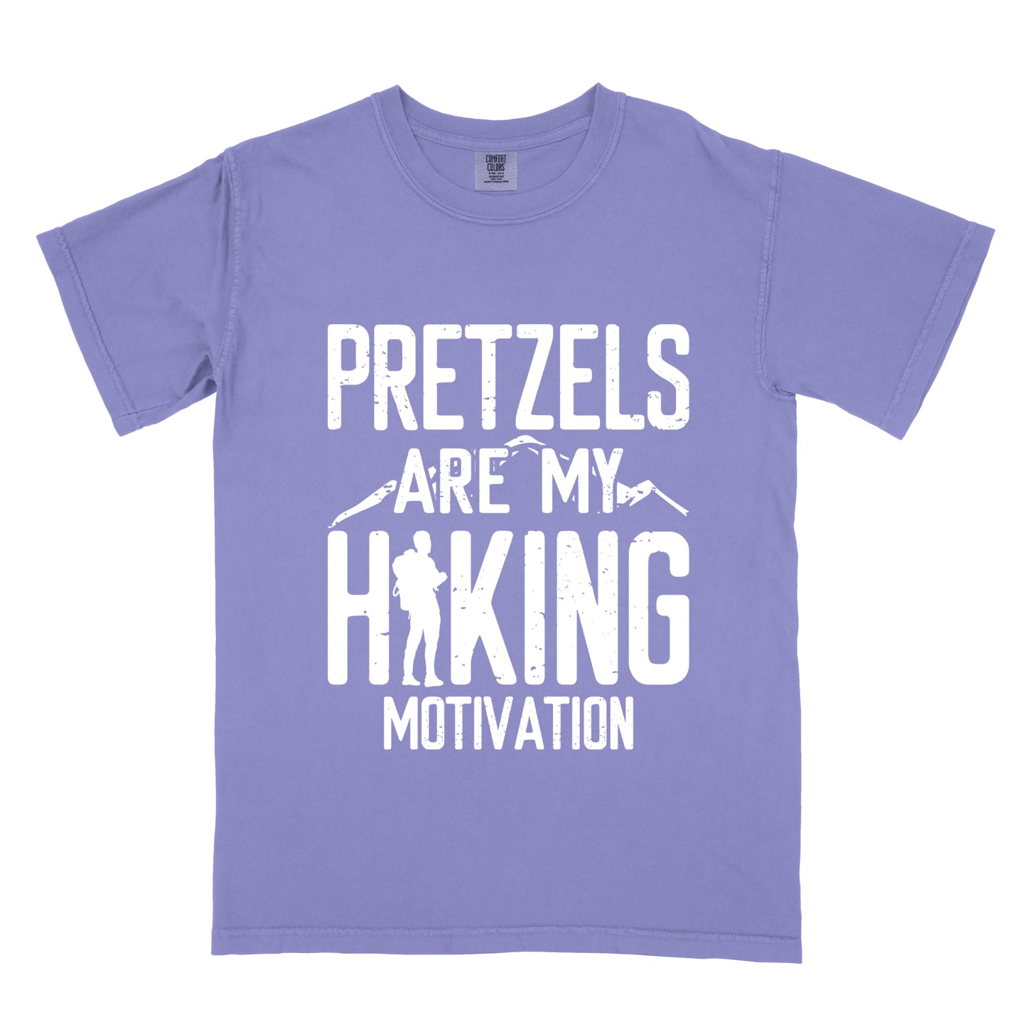 Violet t-shirt with white distressed text reading "PRETZELS ARE MY HIKING MOTIVATION". "PRETZELS" appears at the top, "ARE MY" in the middle with small mountain silhouettes behind it, and "HIKING" in large letters with a hiker silhouette integrated into the letter "H". "MOTIVATION" appears at the bottom.