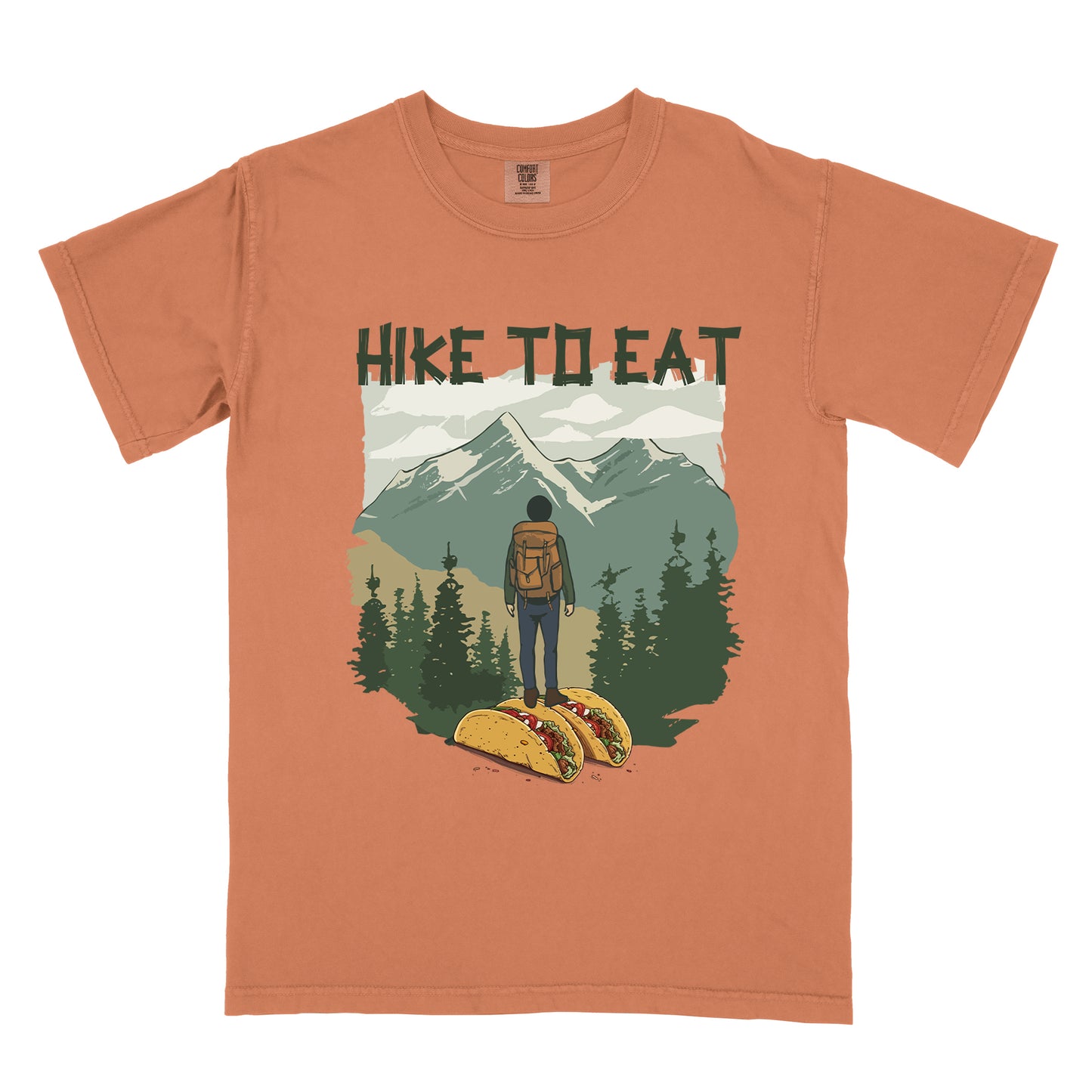 Yam colored (Brown) t-shirt with "HIKE TO EAT" printed at the top in dark green text. The main graphic shows a hiker with backpack standing on two tacos, facing a scenic mountain landscape with pine trees in the foreground and snow-capped peaks in the background.