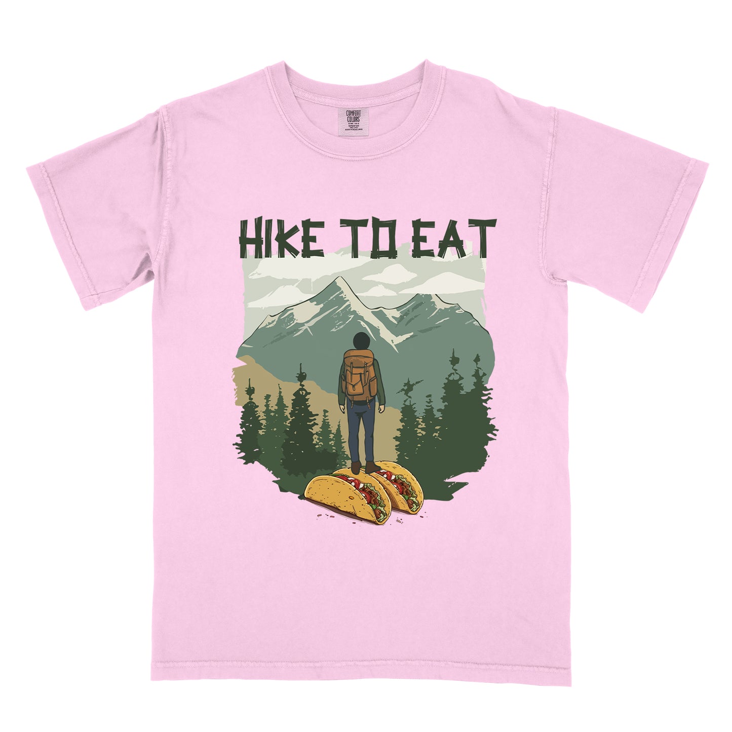Light Pink (Blossom) t-shirt with "HIKE TO EAT" printed at the top in dark green text. The main graphic shows a hiker with backpack standing on two tacos, facing a scenic mountain landscape with pine trees in the foreground and snow-capped peaks in the background.