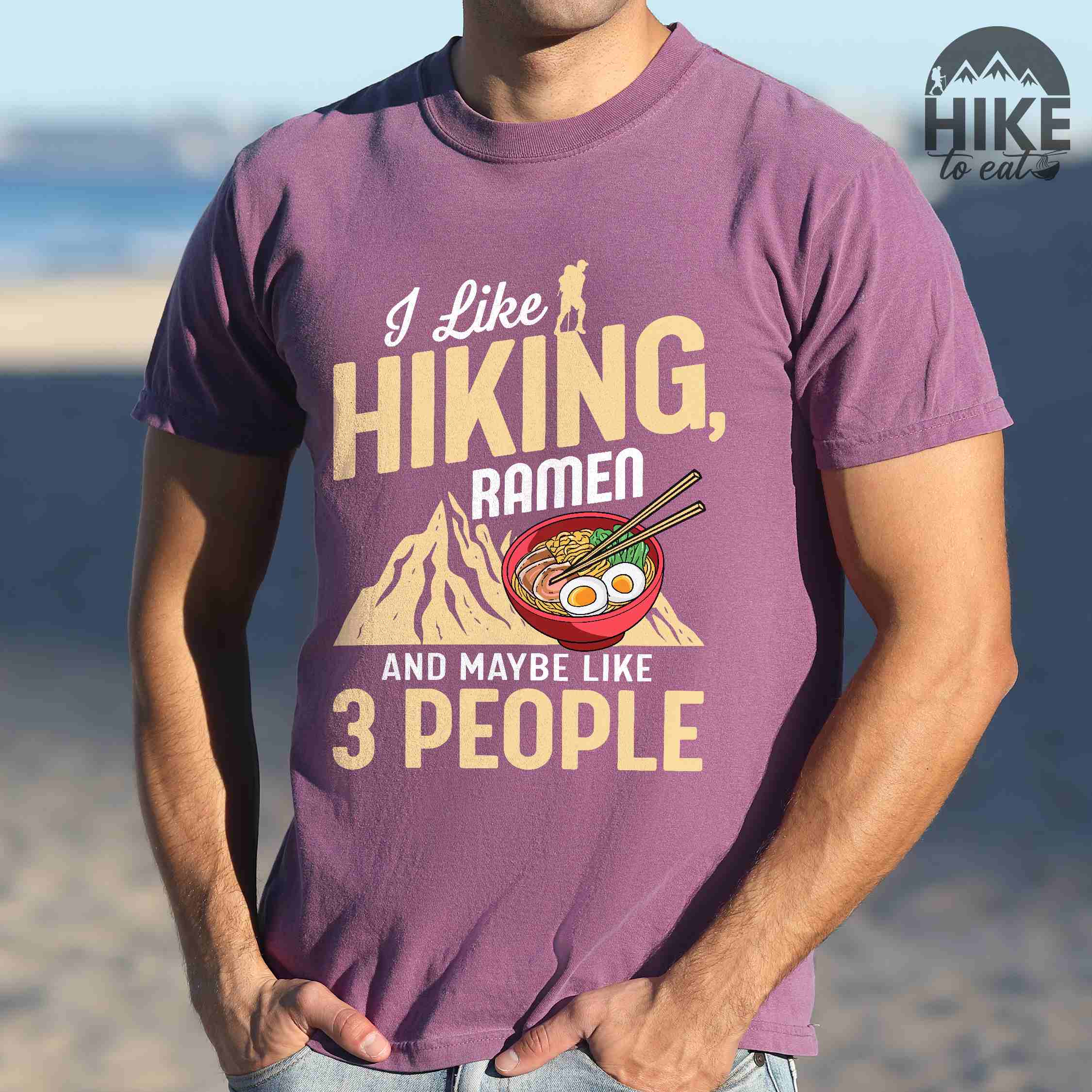 Man wearing berry “Ramen is my Hiking motivation” colored vintage tee with bold text, mountain, Illustration of hot ramen. Perfect tee for a foodie craving for a bowl of ramen,