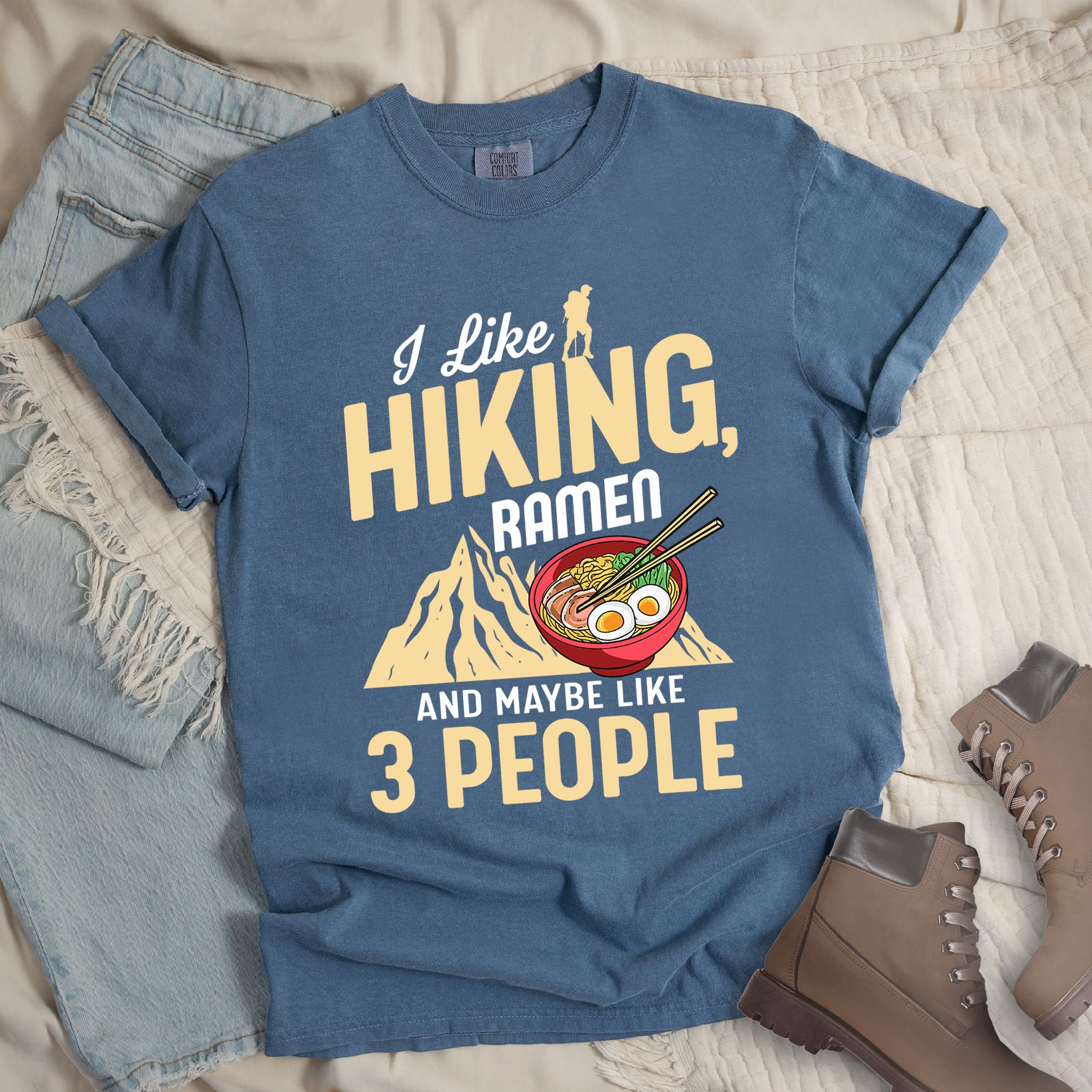 Dark blue shirt with Hiking Design featuring the phrase “I Like Hiking, Ramen, and Maybe Like 3 People” and an illustration of a steaming ramen bowl with chopsticks over a mountain outline.