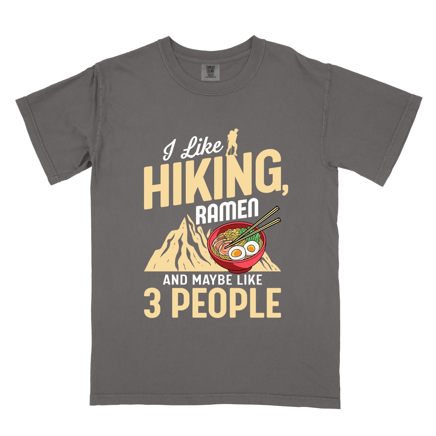 Pepper (Dark Gray) t-shirt with mixed text reading "I Like HIKING, RAMEN AND MAYBE LIKE 3 PEOPLE". "I Like" in white script at top with small gold hiker silhouette, "HIKING," in large gold letters, "RAMEN" in white, and "AND MAYBE LIKE 3 PEOPLE" in white and gold. Features a colorful illustration of a red ramen bowl with eggs, noodles and chopsticks, positioned above a gold mountain silhouette.