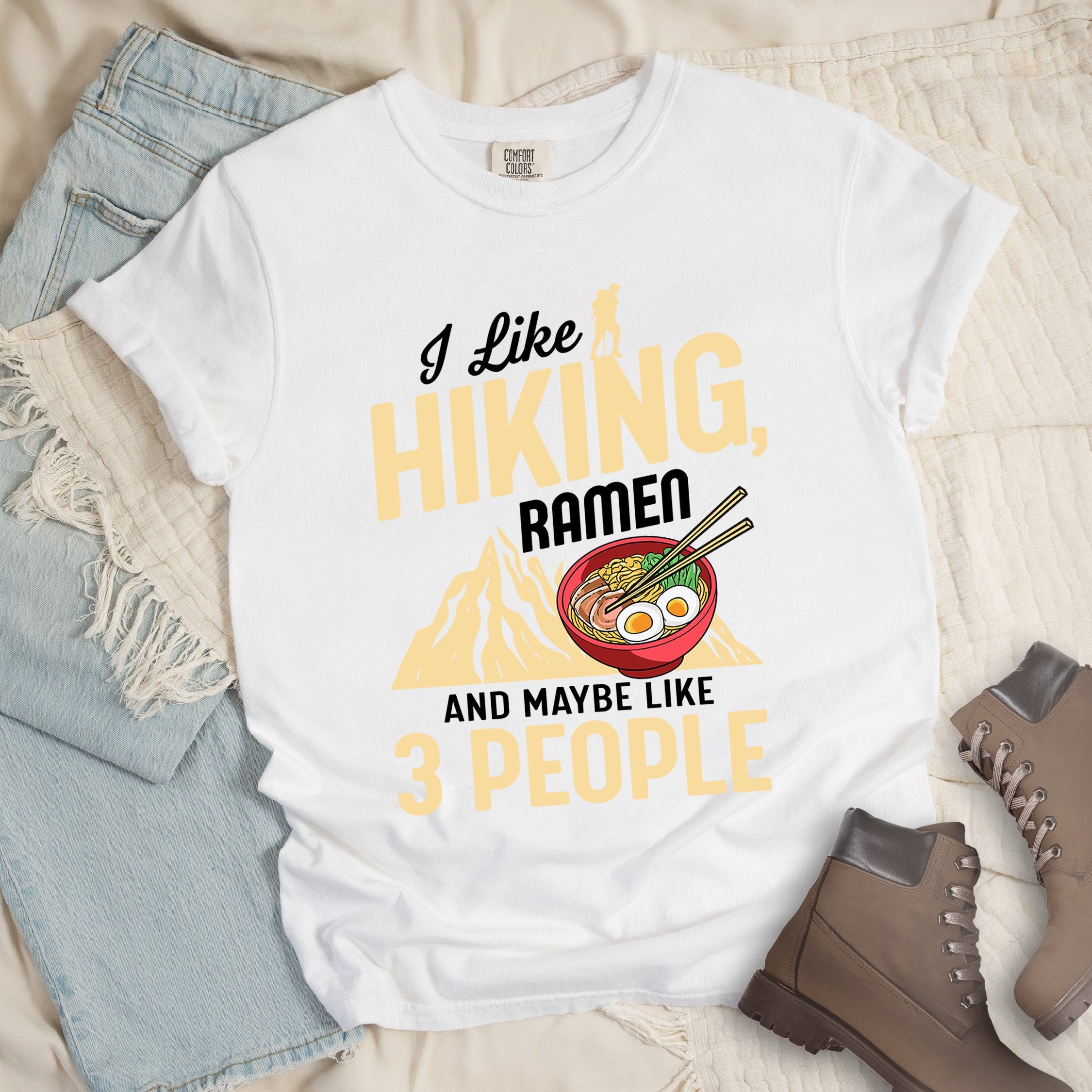 White shirt with Hiking Design featuring the phrase “I Like Hiking, Ramen, and Maybe Like 3 People” and an illustration of a steaming ramen bowl with chopsticks over a mountain outline.