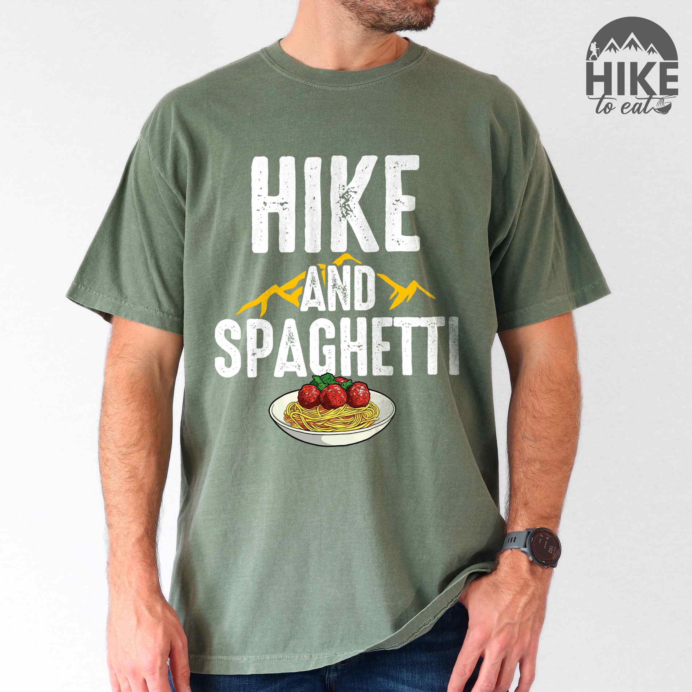 Man wearing moss "Hike and Spaghetti" colored vintage tee with bold typography, birds, mountains, illustrated plate of spaghetti and meatballs, and backpacker for pasta lovers.