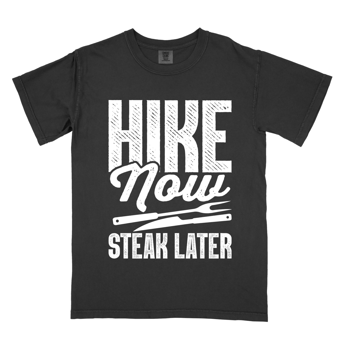 Black t-shirt with white distressed text reading "HIKE Now STEAK LATER". "HIKE" appears in large bold block letters at the top, "Now" in stylish script in the middle, and "STEAK LATER" in block letters at the bottom. Between the middle and bottom text is a simple illustration of a steak knife. The design emphasizes the reward of enjoying steak after completing a hiking activity.