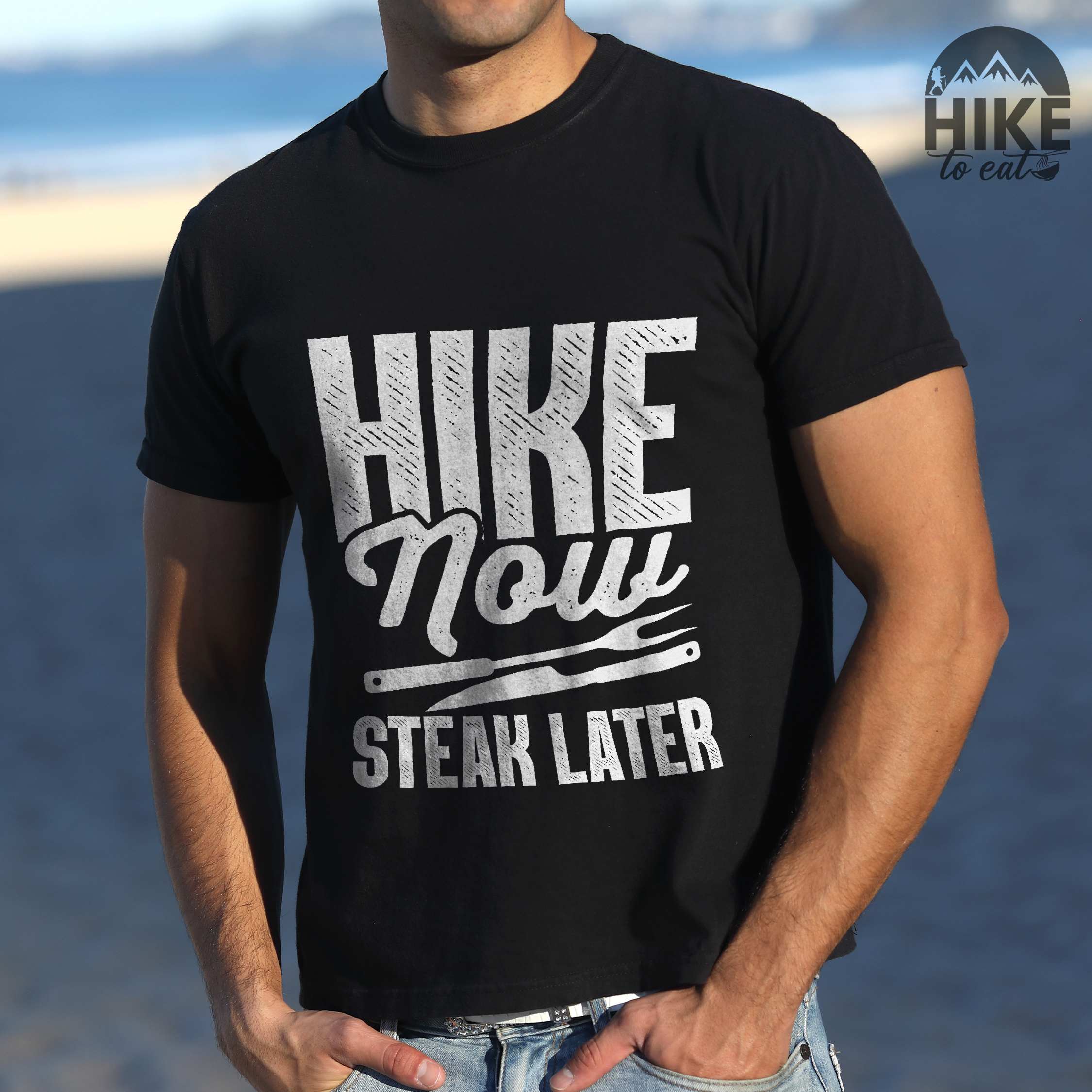 Man wearing black "Hike now steak later" colored vintage tee with bold typography, illustrated steak utensils, and backpacker for steak lovers.