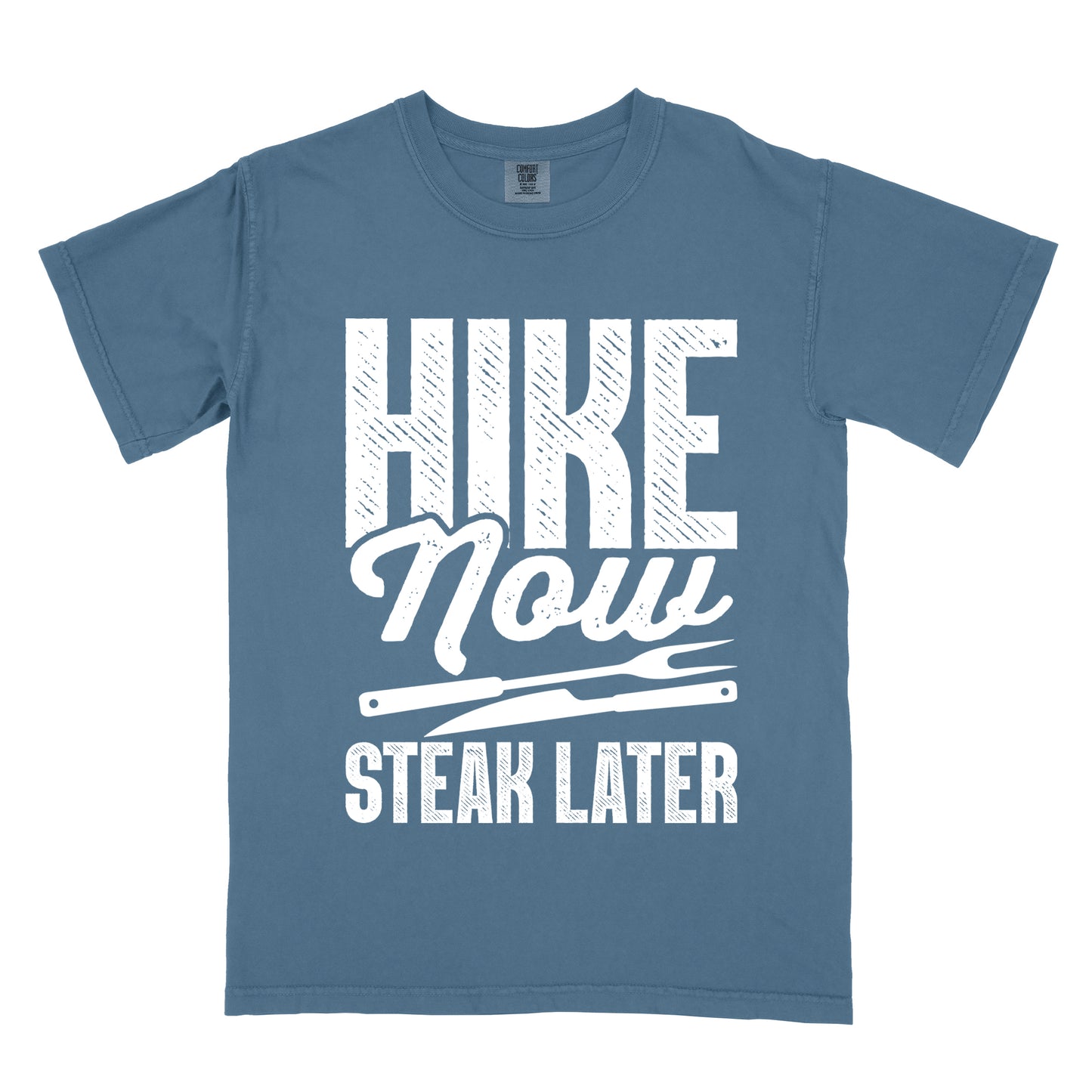 Blue Jean (Denim Blue) t-shirt with white distressed text reading "HIKE Now STEAK LATER". "HIKE" appears in large bold block letters at the top, "Now" in stylish script in the middle, and "STEAK LATER" in block letters at the bottom. Between the middle and bottom text is a simple illustration of a steak knife. The design emphasizes the reward of enjoying steak after completing a hiking activity.