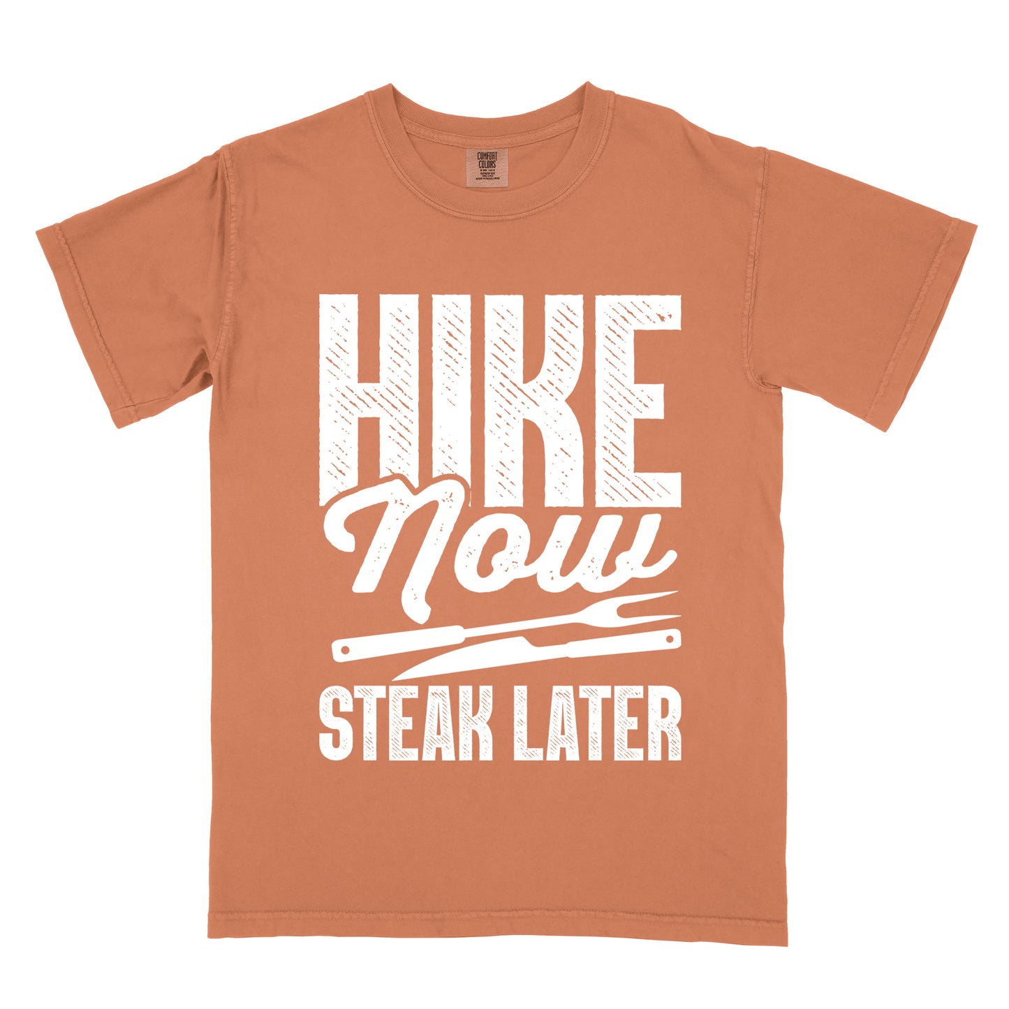 Yam (Brown) t-shirt with white distressed text reading "HIKE Now STEAK LATER". "HIKE" appears in large bold block letters at the top, "Now" in stylish script in the middle, and "STEAK LATER" in block letters at the bottom. Between the middle and bottom text is a simple illustration of a steak knife. The design emphasizes the reward of enjoying steak after completing a hiking activity.