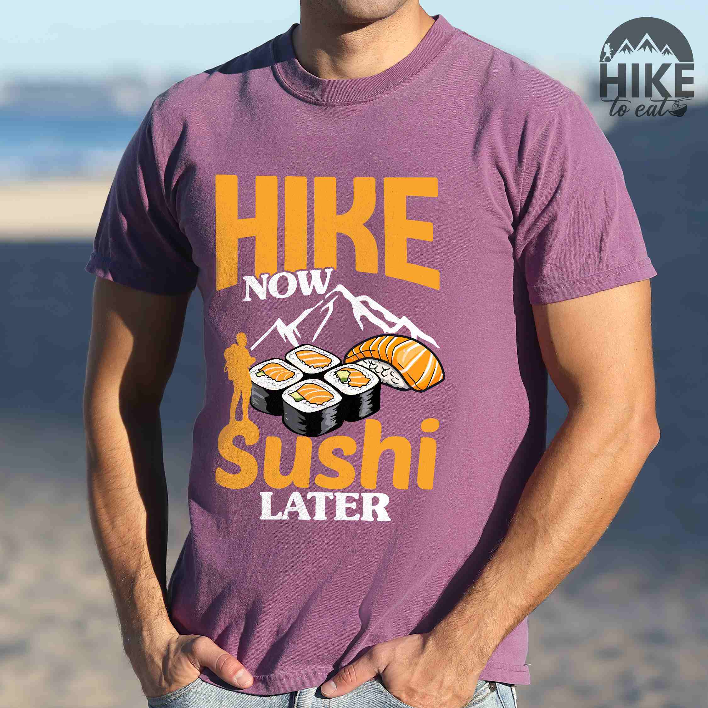 Man wearing berry "Hike now sushi later" colored vintage tee with bold typography, birds, mountains, illustrated sushi platter, and backpacker for sushi lovers.