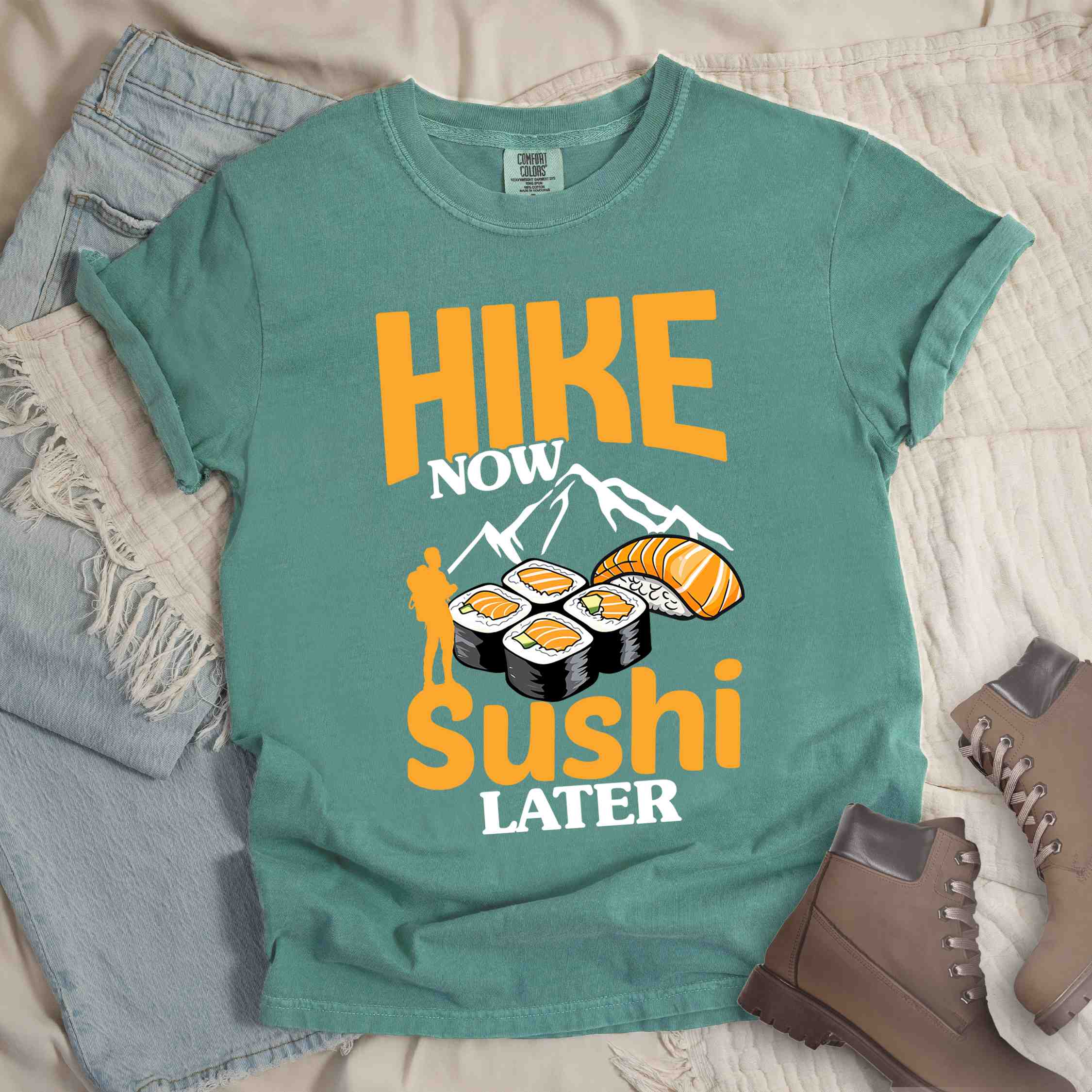 Light green "Hike now sushi later" colored vintage tee with bold typography, birds, mountains, illustrated sushi platter, and backpacker for sushi lovers.
