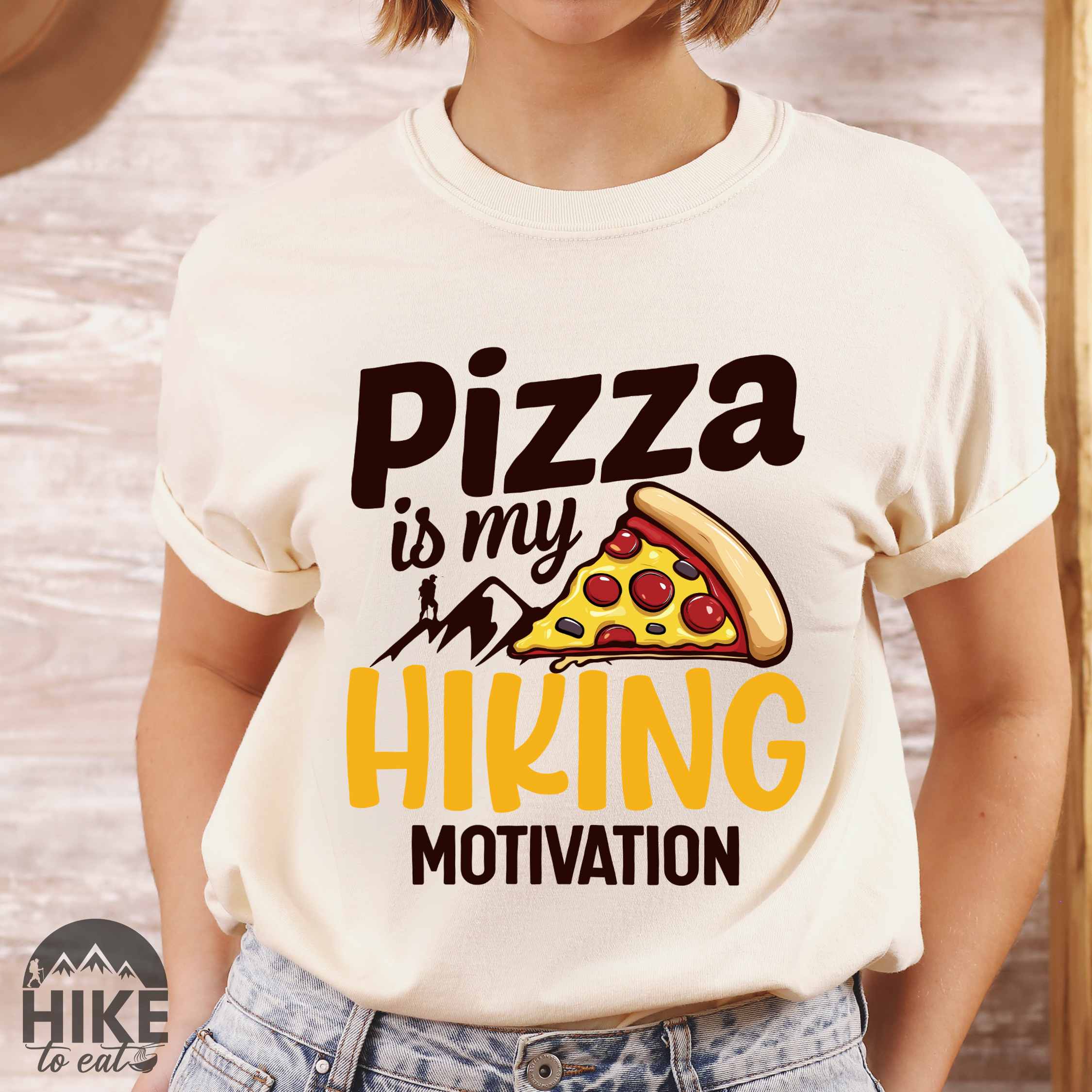 Woman wearing ivory "Pizza is my hiking motivation" colored vintage tee with bold typography, birds, mountains, illustrated pizza slice, and backpacker for pizza lovers.