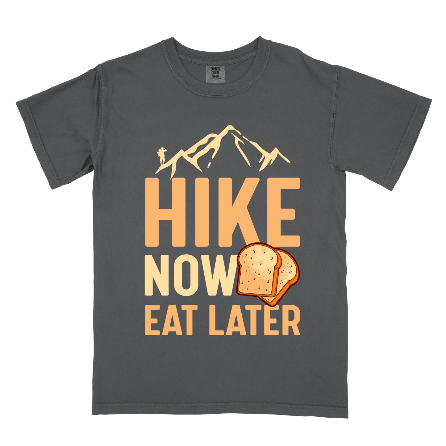 A Graphite (Deep Gray) t-shirt with a design showing "HIKE NOW EAT LATER" in gradient orange and tan text. Above "HIKE" is a mountain silhouette with a small hiker figure. A sandwich/toast illustration appears between "NOW" and "EAT LATER". The text is arranged in three lines with "HIKE" at the top in largest font, followed by "NOW" and "EAT LATER" below.