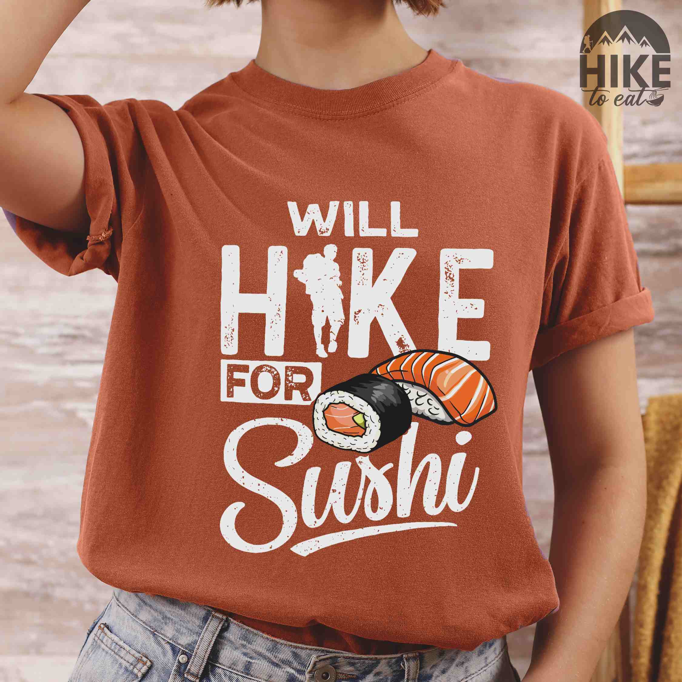 Woman wearing yam "Will hike for sushi" colored vintage tee with bold typography, birds, mountains, illustrated sushi platter, and backpacker for sushi lovers.