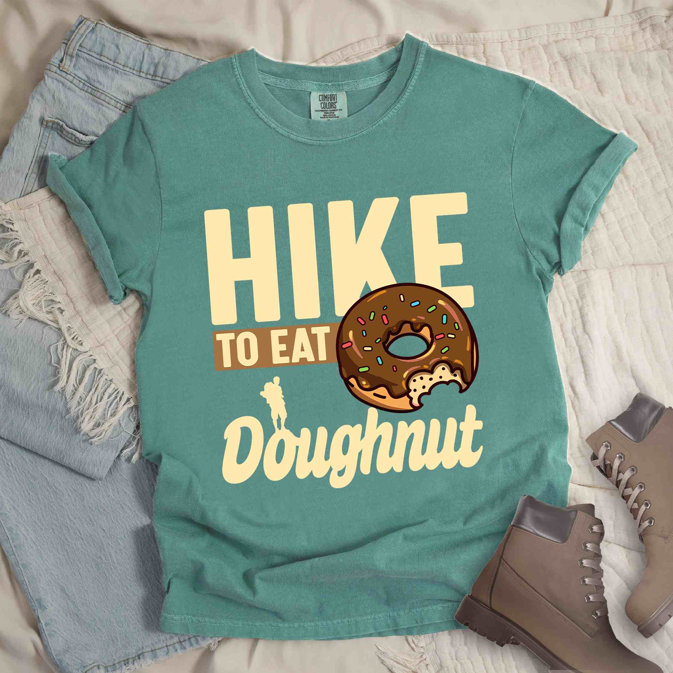 Light green "Hike to eat doughnut" colored vintage tee with bold typography, birds, mountains, illustrated baked chocolate glazed donut, and backpacker for donut lovers.