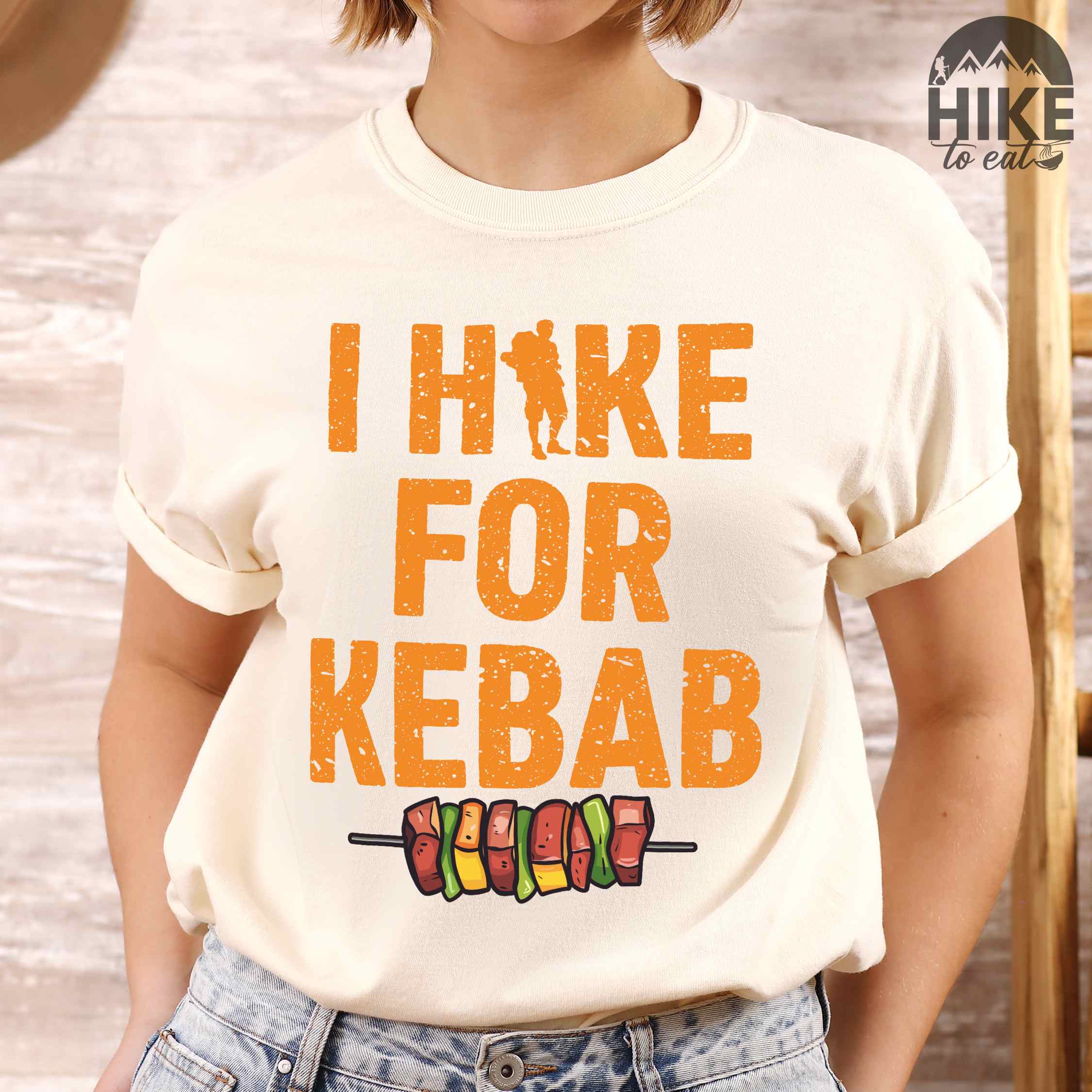 Woman wearing ivory "I hike for kebab" colored vintage tee with bold typography illustrated grilled kebabt, and backpacker for kebab lovers.