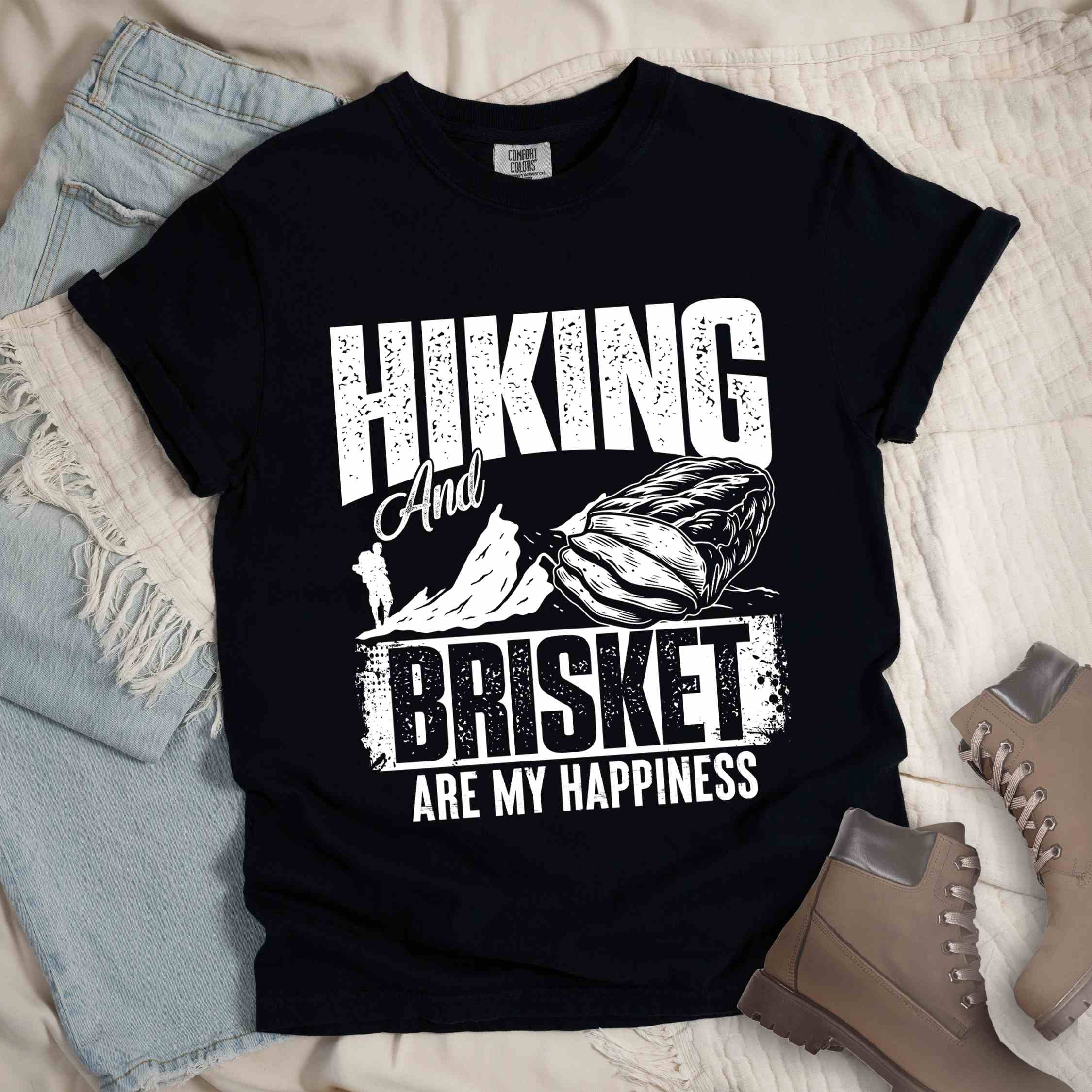 Black "hiking and brisket are my happiness" colored vintage tee with bold typography, birds, mountains, illustrated bbq beef brisket, and backpacker for bbq lovers.