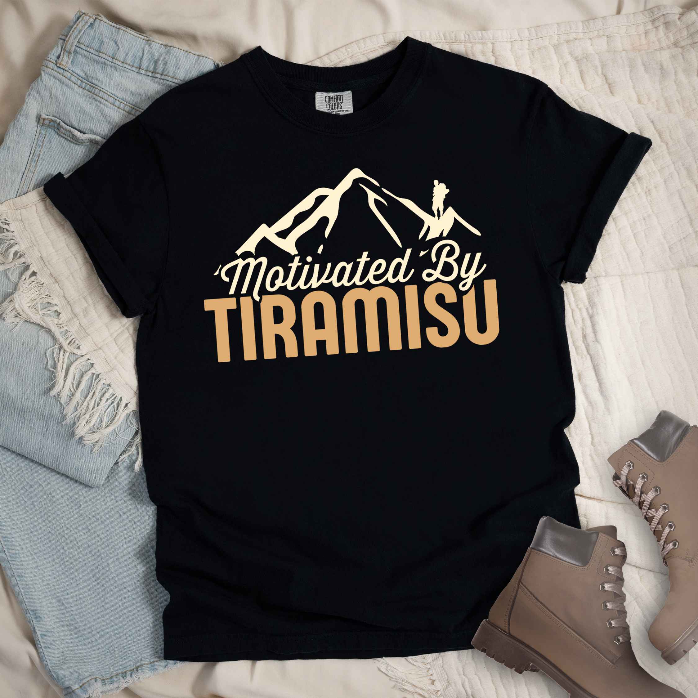 Black "Motivated by Tiramisu" colored vintage tee with bold typography, mountains, and backpackers with a sweet tooth.