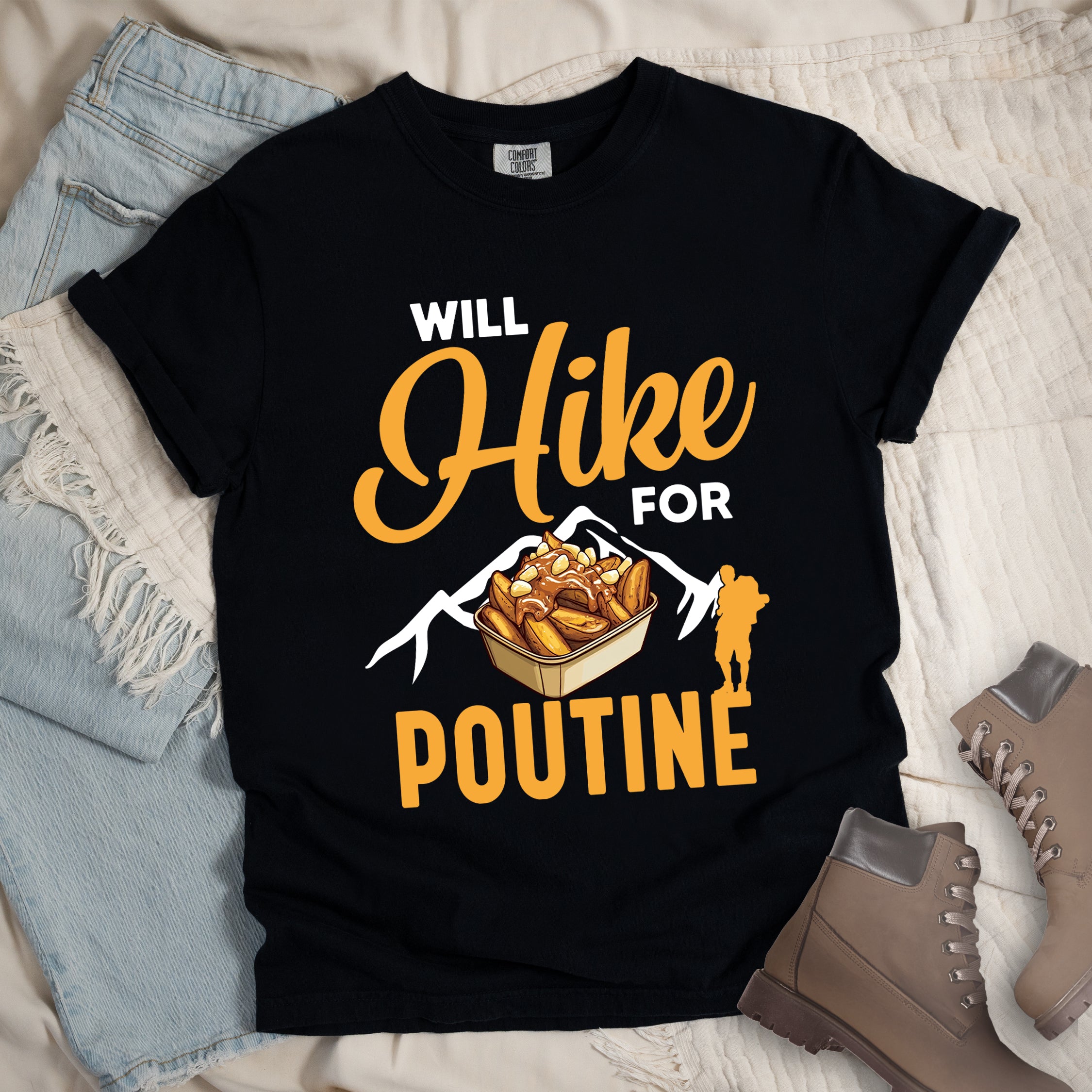 Black t-shirt with orange and white text reading "WILL Hike FOR POUTINE". "WILL" appears in white at the top, "Hike" in large orange script in the middle, "FOR" in white, and "POUTINE" in large orange letters at the bottom. Features a detailed illustration of a container of poutine (french fries with cheese curds and gravy) in the center, white mountain silhouettes behind it, and an orange hiker silhouette on the right.