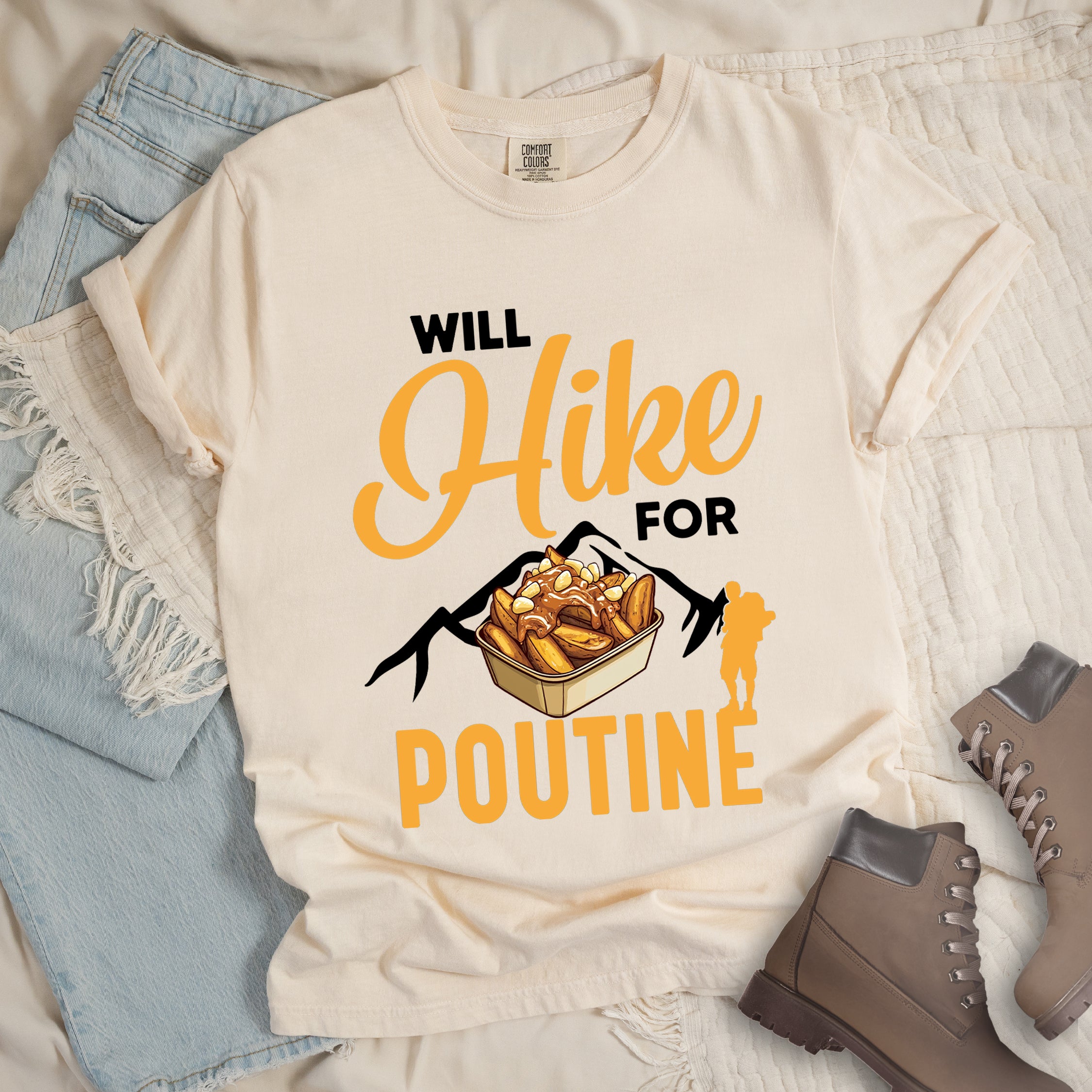 Ivory (Cream White) t-shirt with orange and black text reading "WILL Hike FOR POUTINE". "WILL" appears in black at the top, "Hike" in large orange script in the middle, "FOR" in black, and "POUTINE" in large orange letters at the bottom. Features a detailed illustration of a container of poutine (french fries with cheese curds and gravy) in the center, black mountain silhouettes behind it, and an orange hiker silhouette on the right.